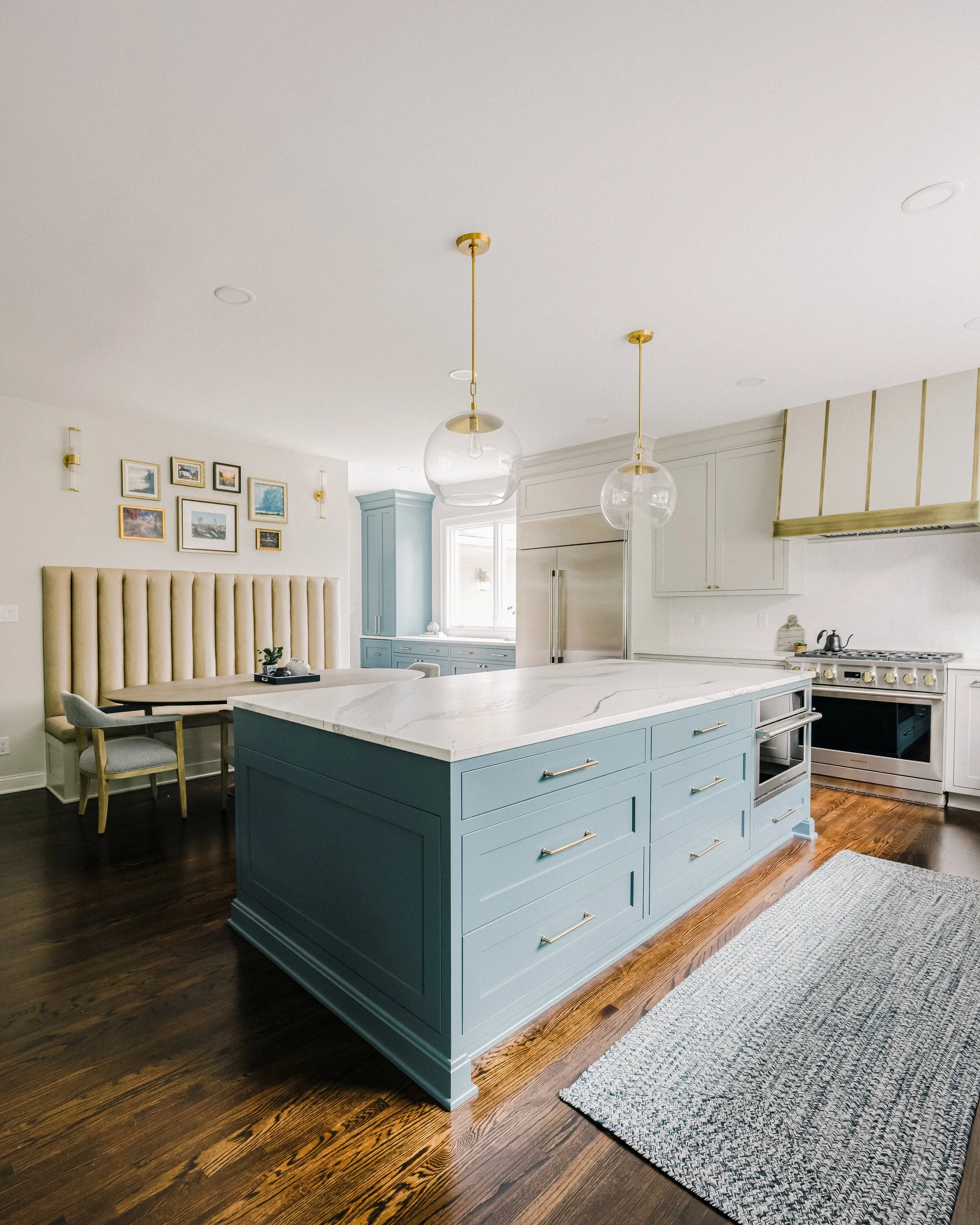 Modern, open kitchen with a ten-foot, stunning blue island, Cambria quartz countertop, and Visual Comfort pendant lights. Cozy dining nook with Banquette bench and framed art on walls.