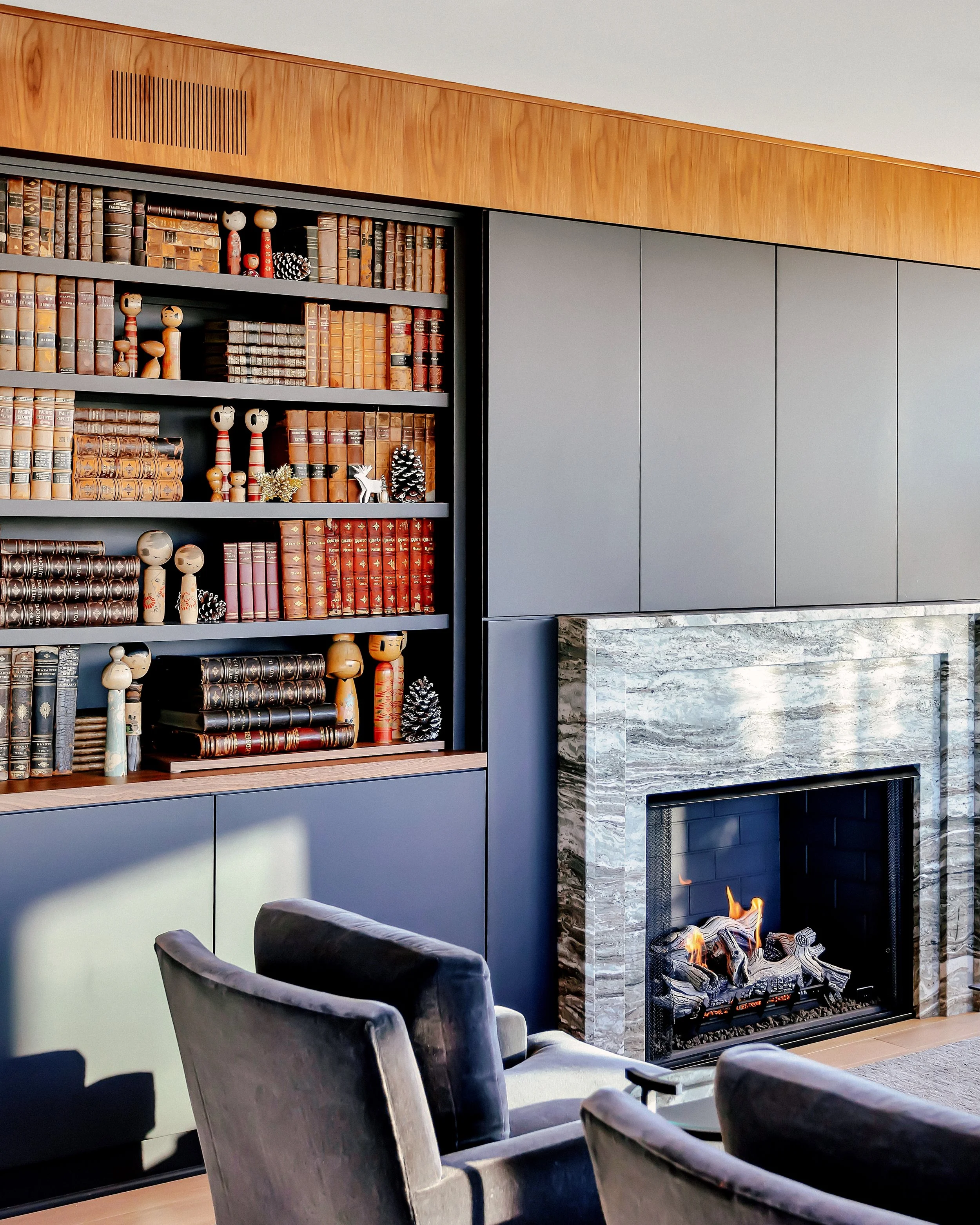 A modern living room space with a striking stone fireplace, library wall, and deep wood accents.