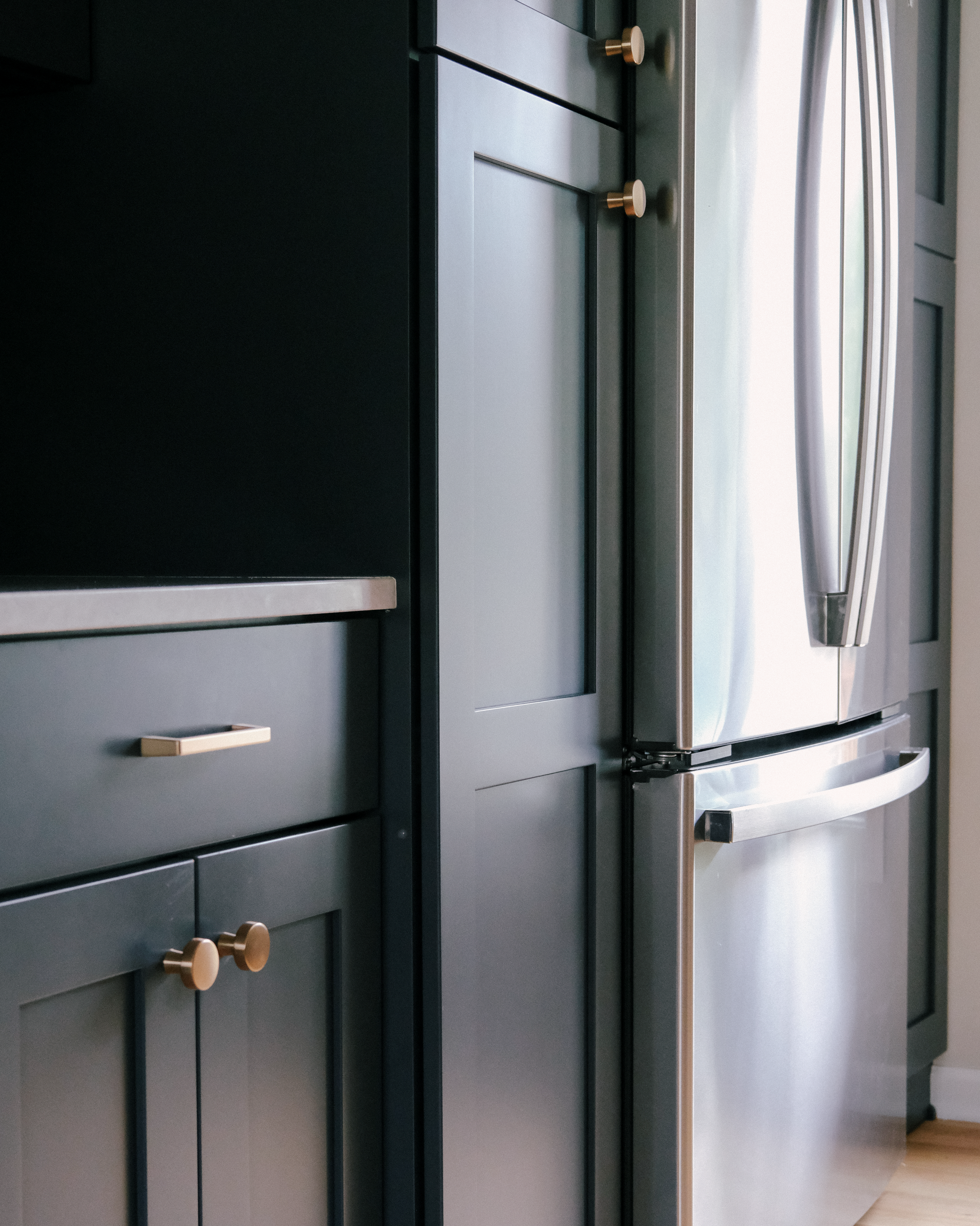 Modern kitchen with sleek, blue cabinetry, gold hardware accents and a stainless steel refrigerator.
