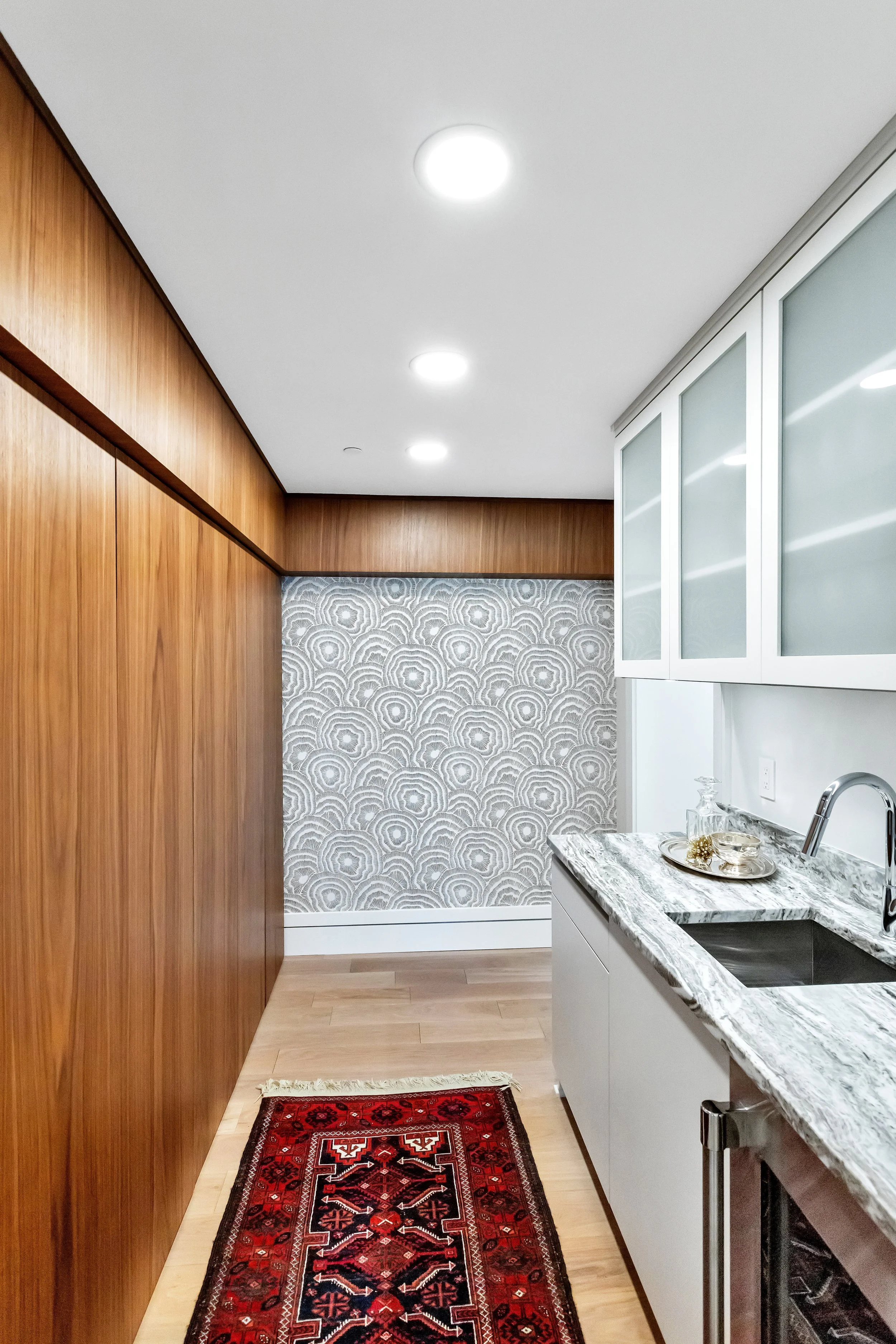 Modern interior with warm wood paneling and white textured wallpaper. A chic wet bar and part of a red rug peek into the frame, creating a cozy feel.