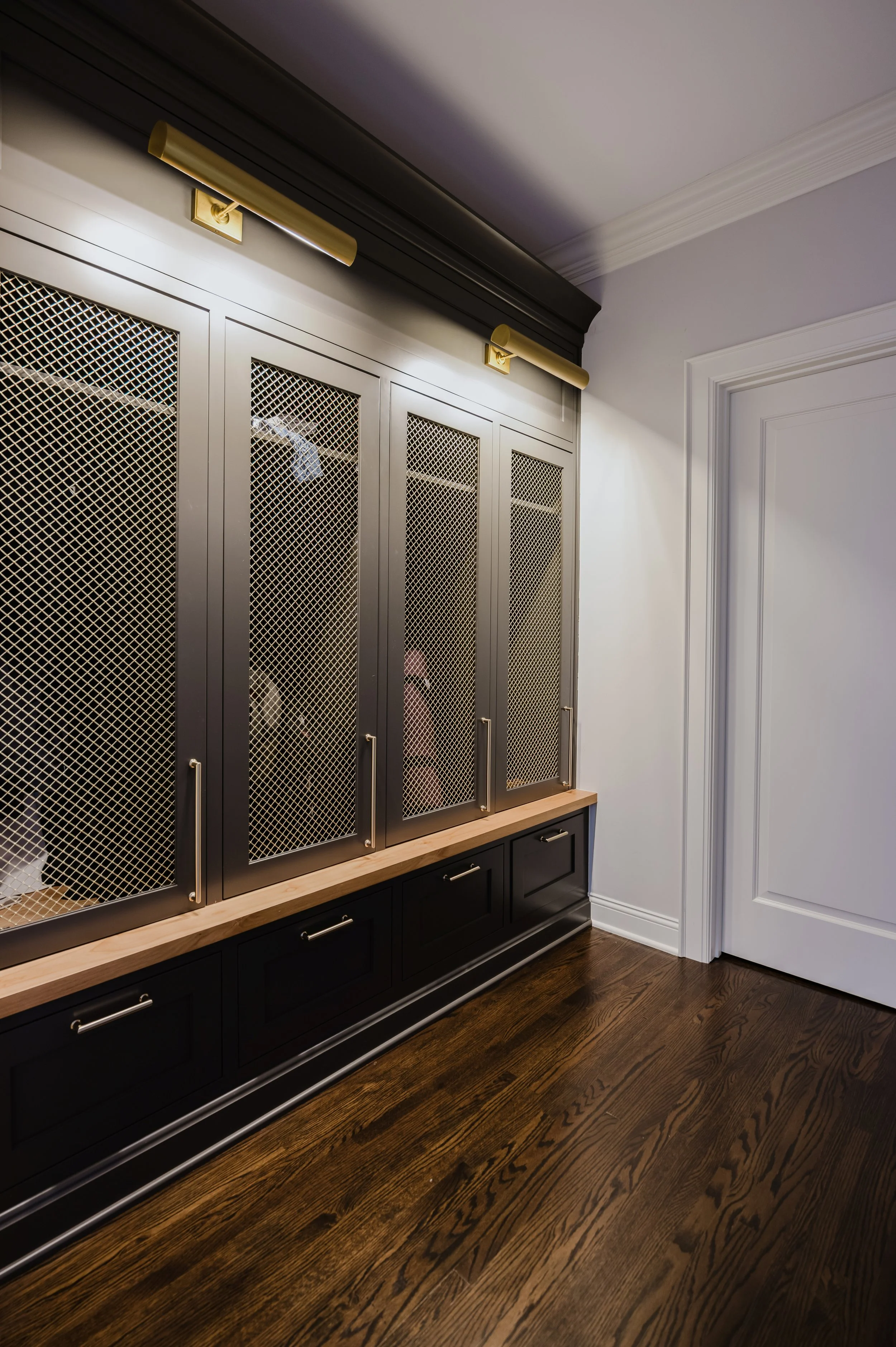 Moody metal lockers with mesh-front doors and gold accents on handles and upper lighting fixtures line a mudroom.