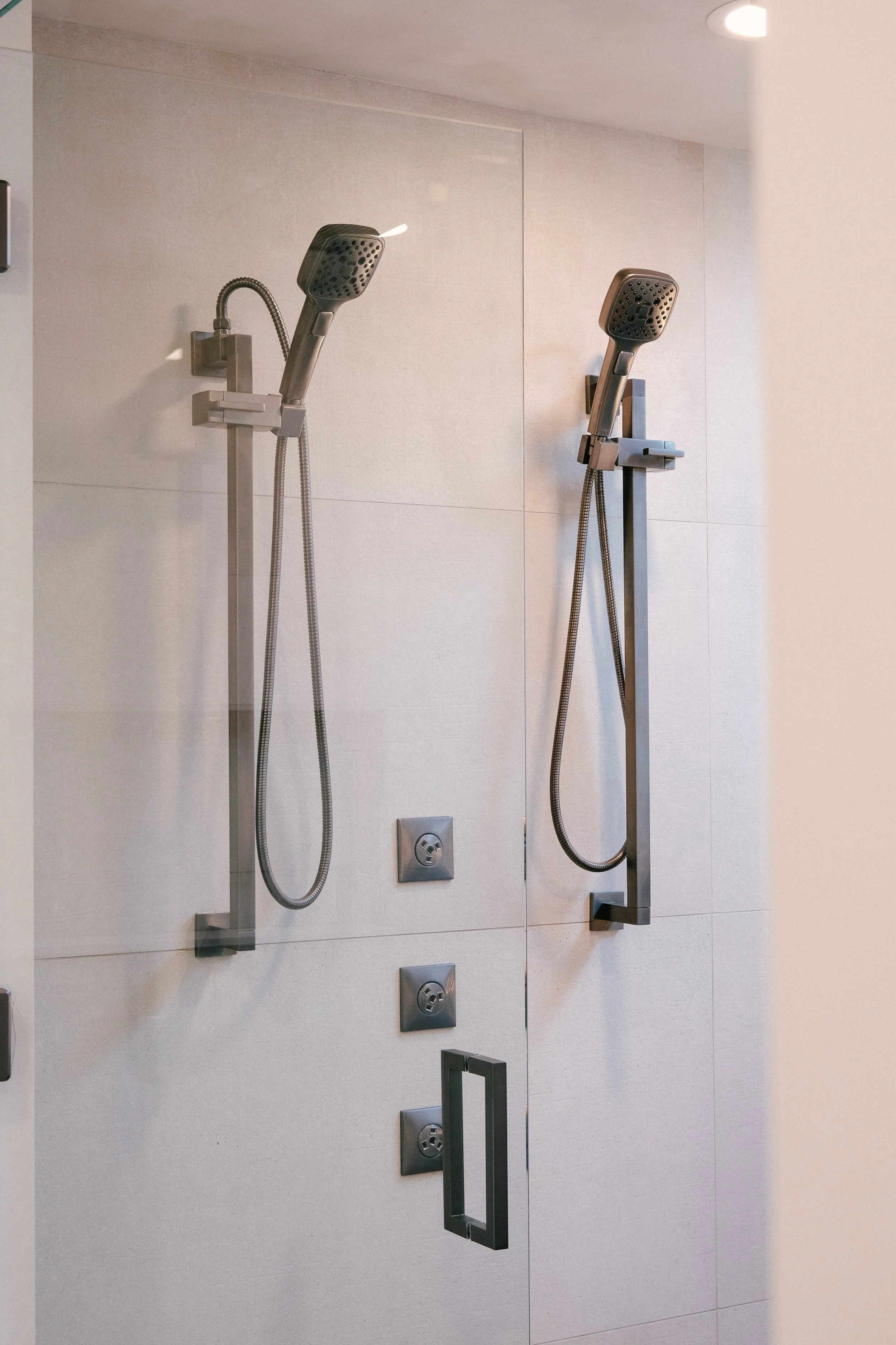 Modern shower with dual adjustable hand-showers from Brizo, sleek luxe steel finish, and minimalist wall controls, conveying a clean, contemporary aesthetic.