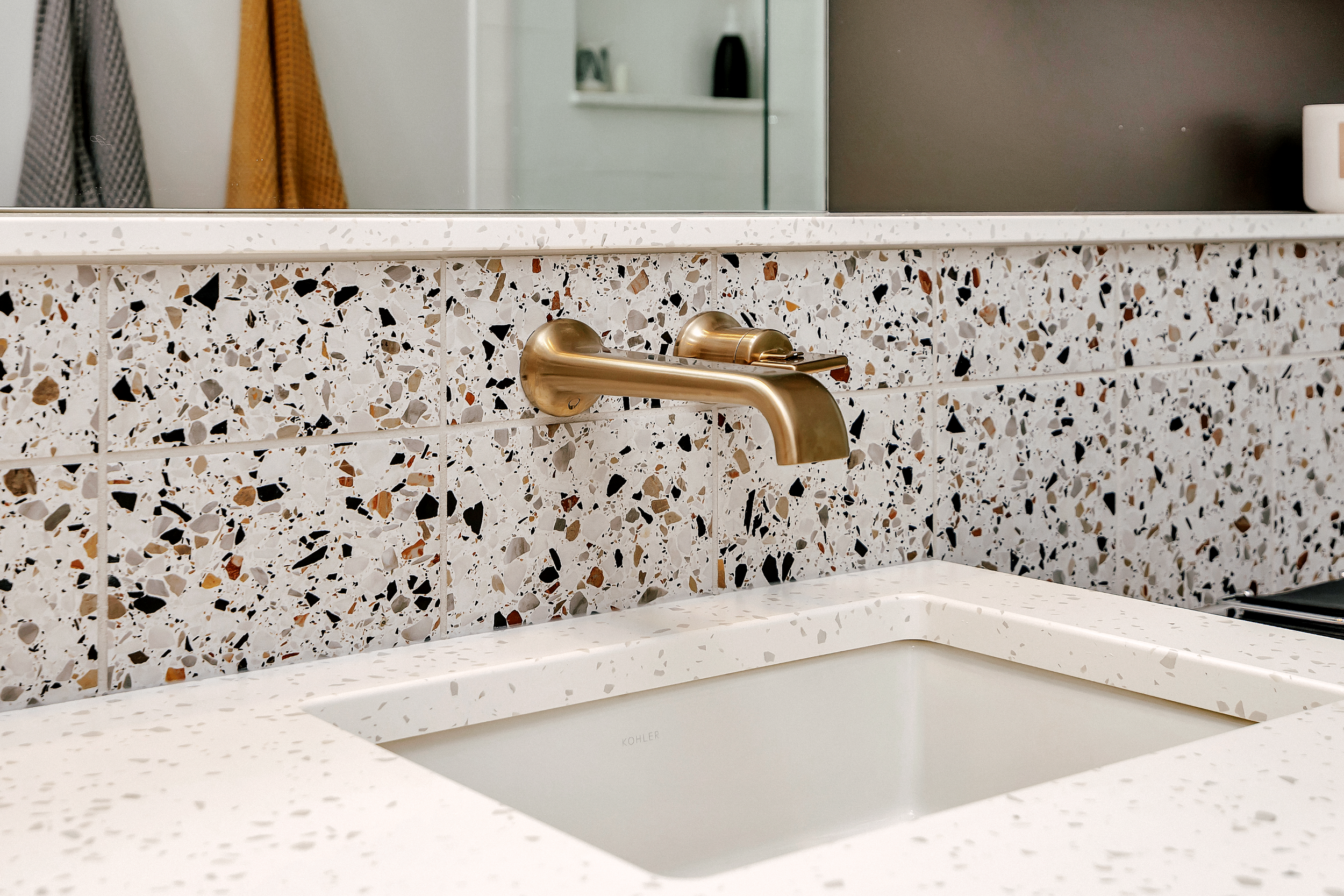 Modern bathroom sink with a white quartz countertop and backsplash, featuring a mosaic of colors. A sleek broze faucet adds elegance to the design.