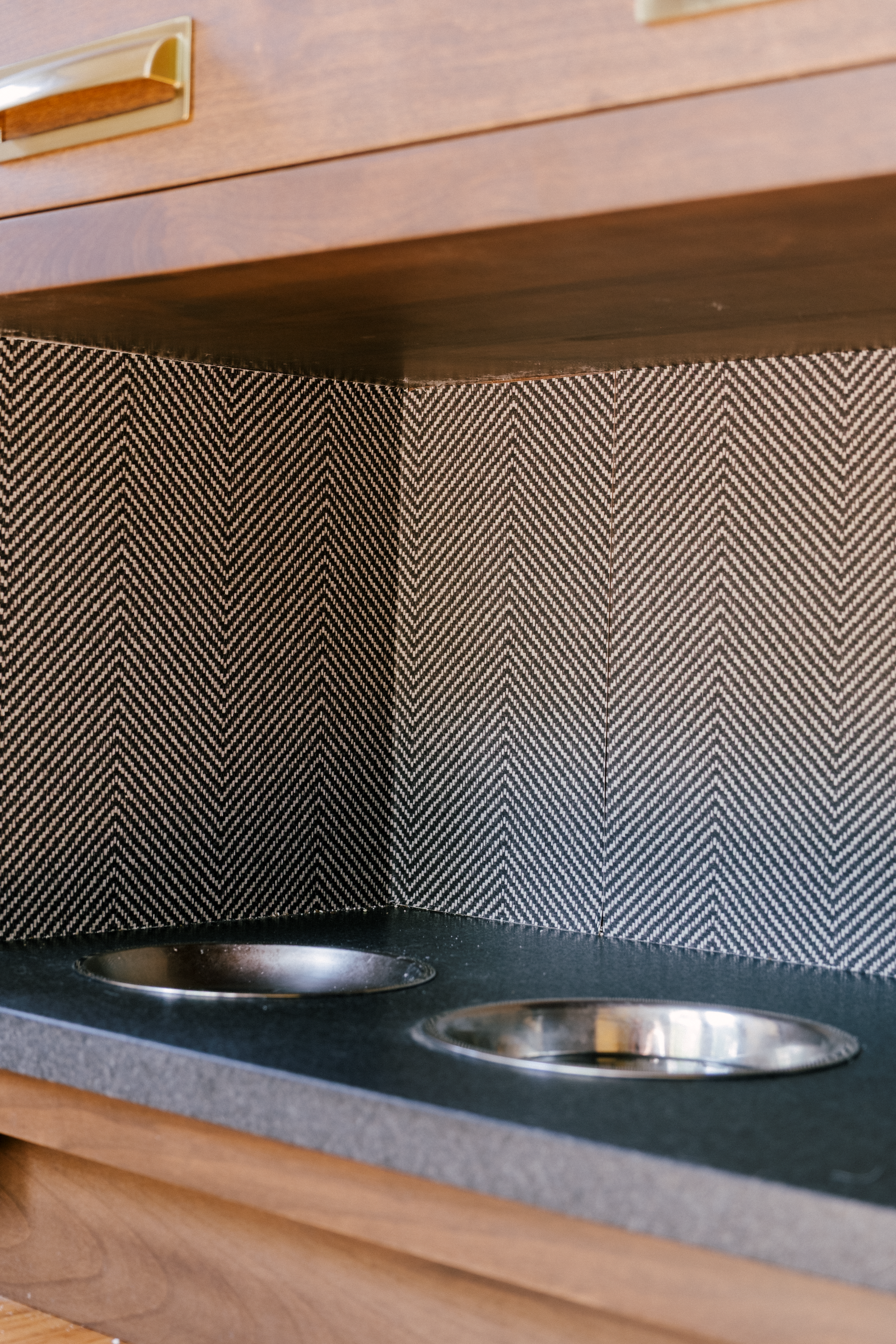 A built-in dog station with stainless steel food and drink bowls features a herringbone vinyl wallpaper as a creative accent.