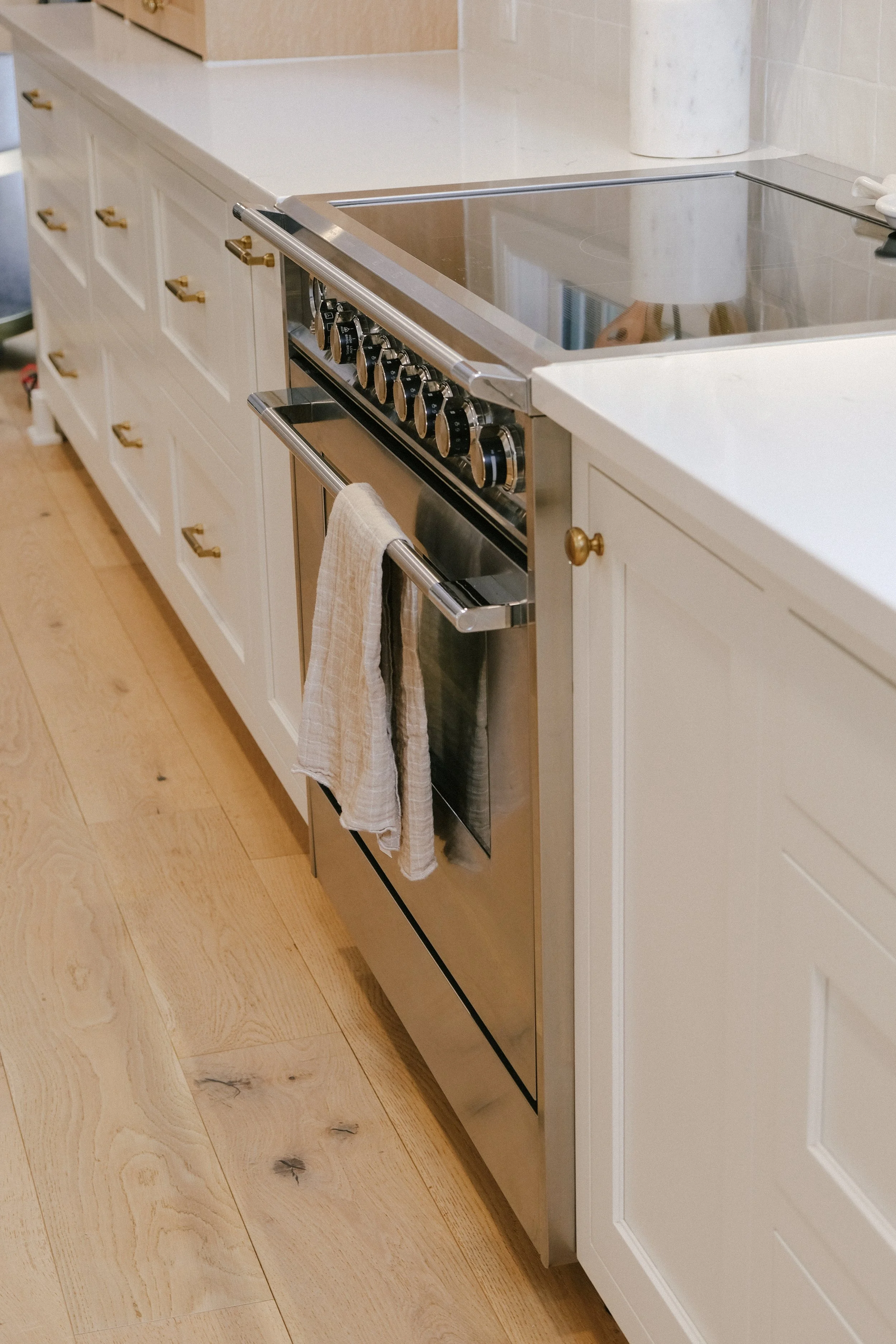Neutral, modern kitchen with a high-end range, adorned with a white towel. Surrounding custom cabinetry and light wood floor create a clean, warm ambiance.