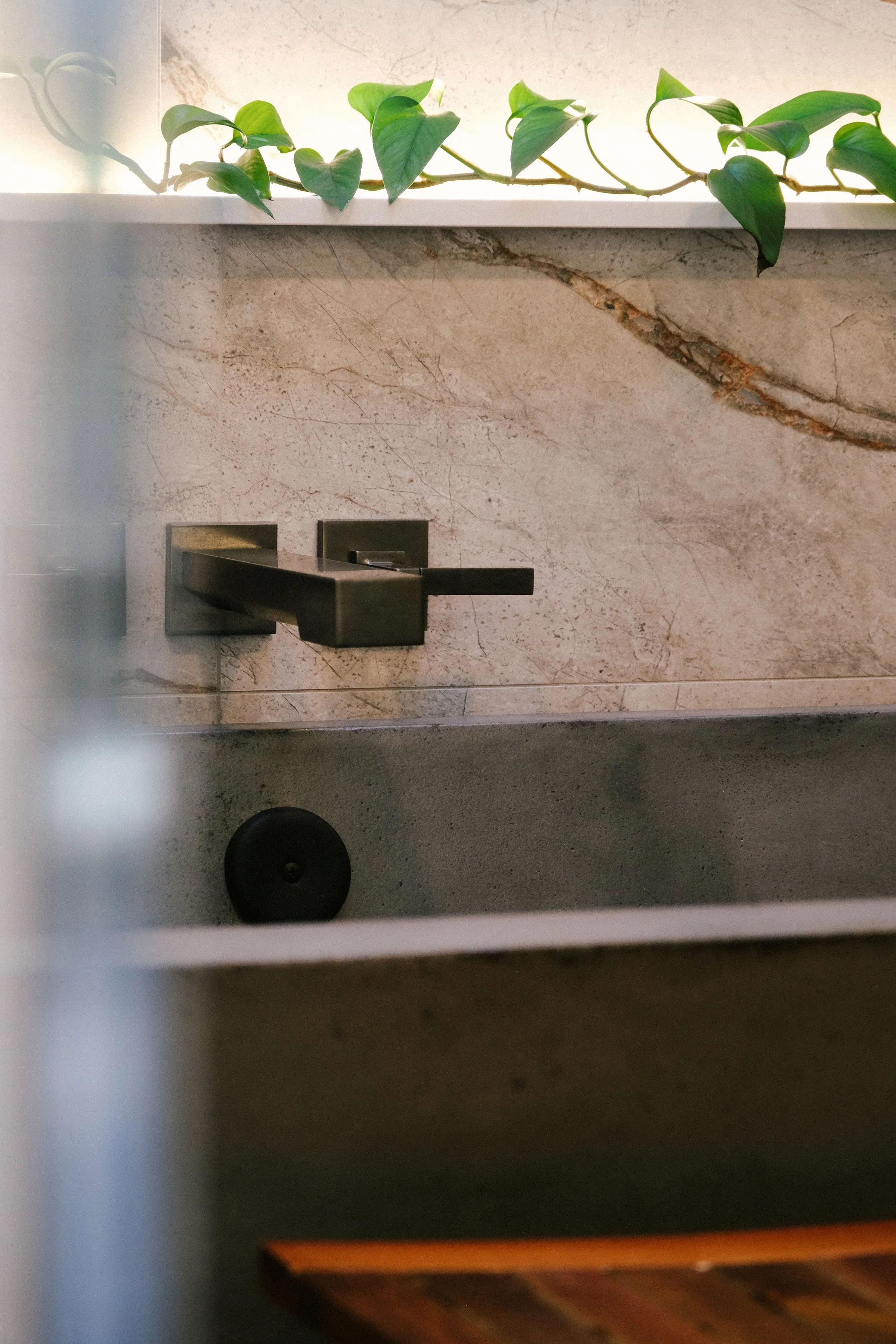 Bathroom scene with a modern wall-mounted Frank Lloyd Wright faucet on a stunning stone shower wall with veining. A leafy vine decorates the top, adding naturalism and elegance.