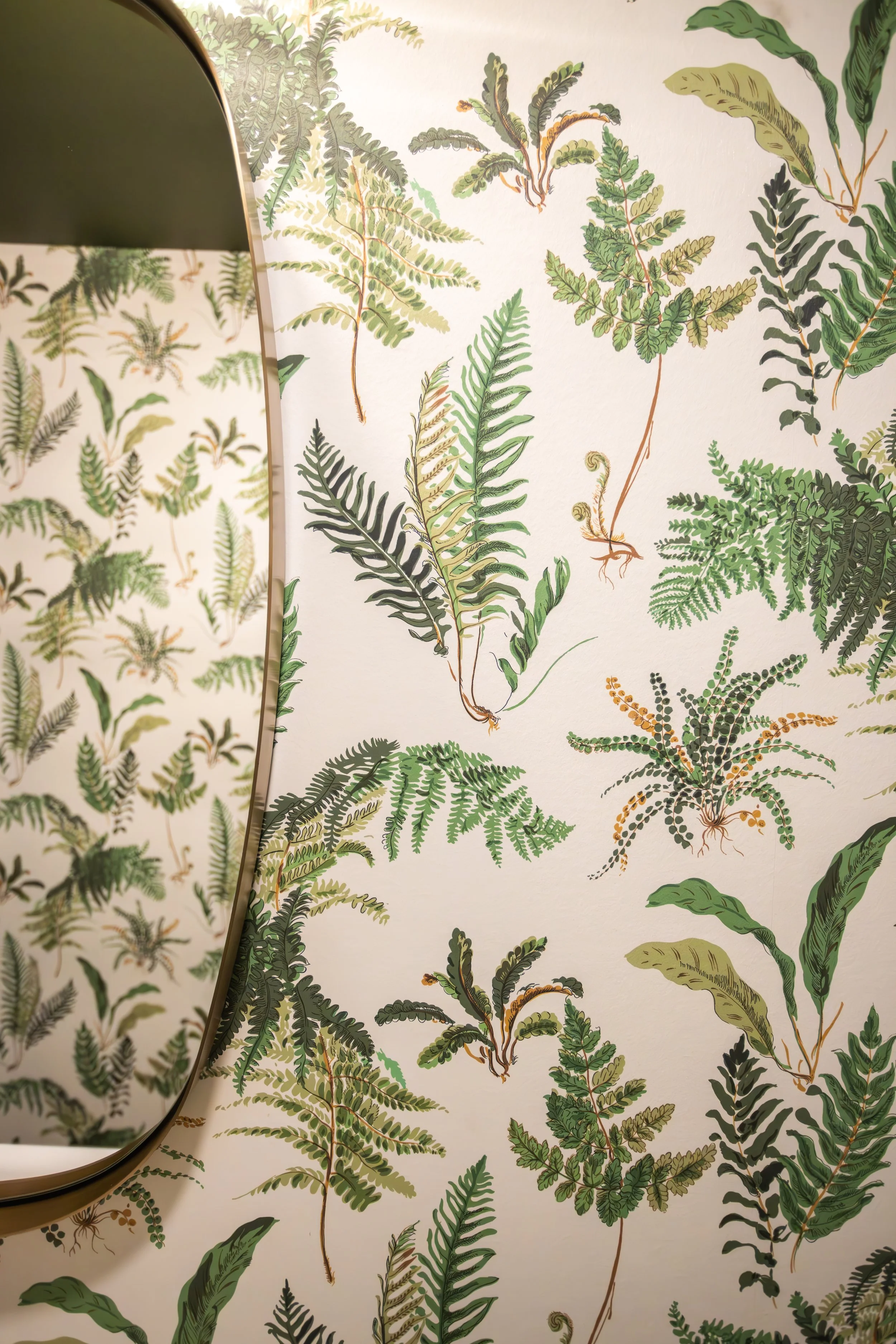 A lush green botanical wallpaper surrounding a gold-rimmed mirror.