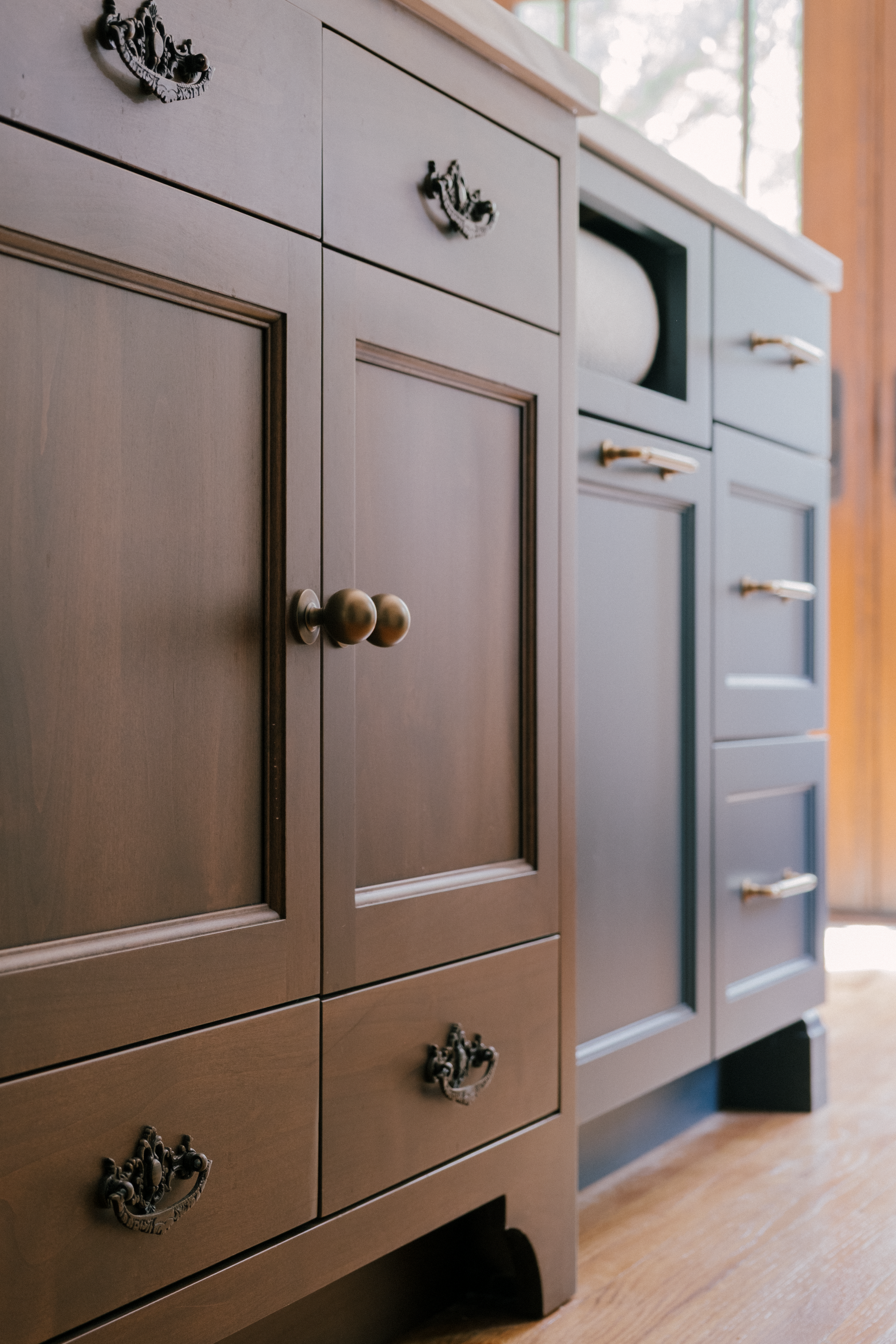 An antique sink basin with weathered hardware next to modern blue custom cabinets. The blue cabinets are adorned by an integrated paper towel rack and honey bronze hardware.