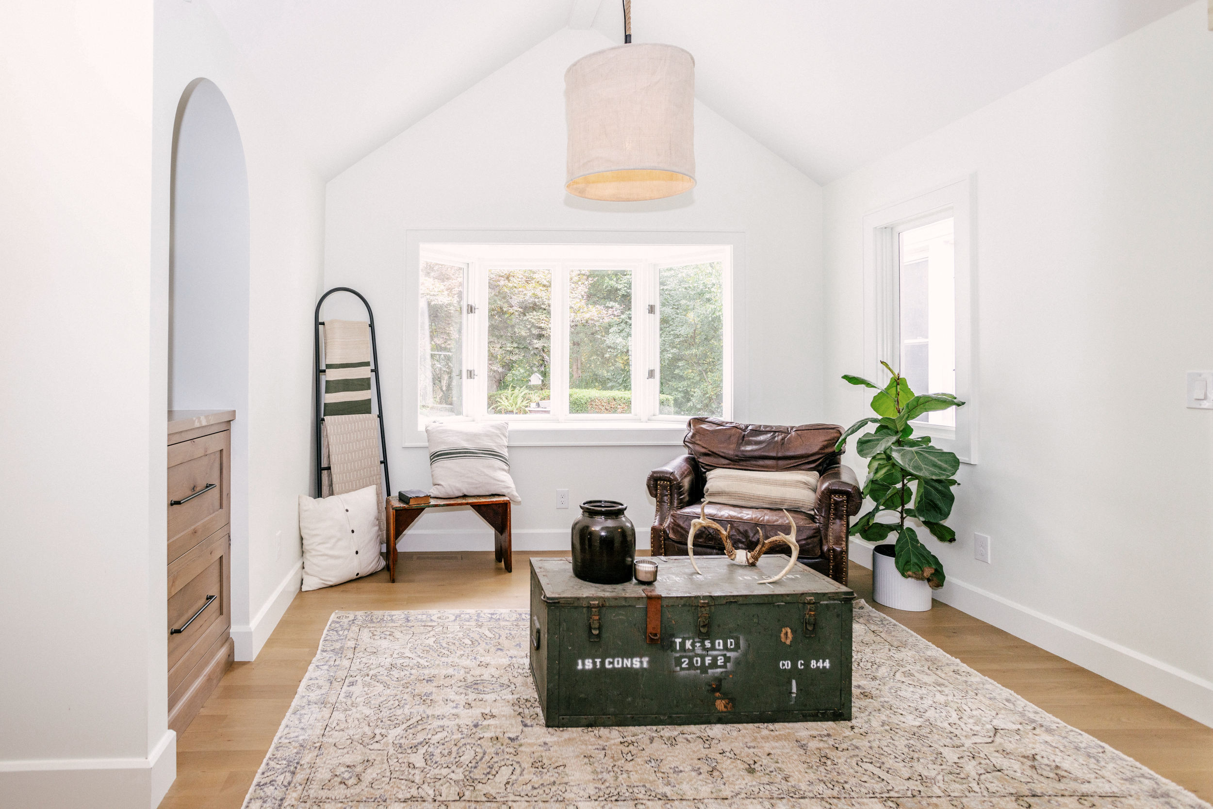 Cozy living room with a vintage trunk as a coffee table, topped with decor. A leather armchair, record player niche, and warm, neutral tones create a welcoming atmosphere.