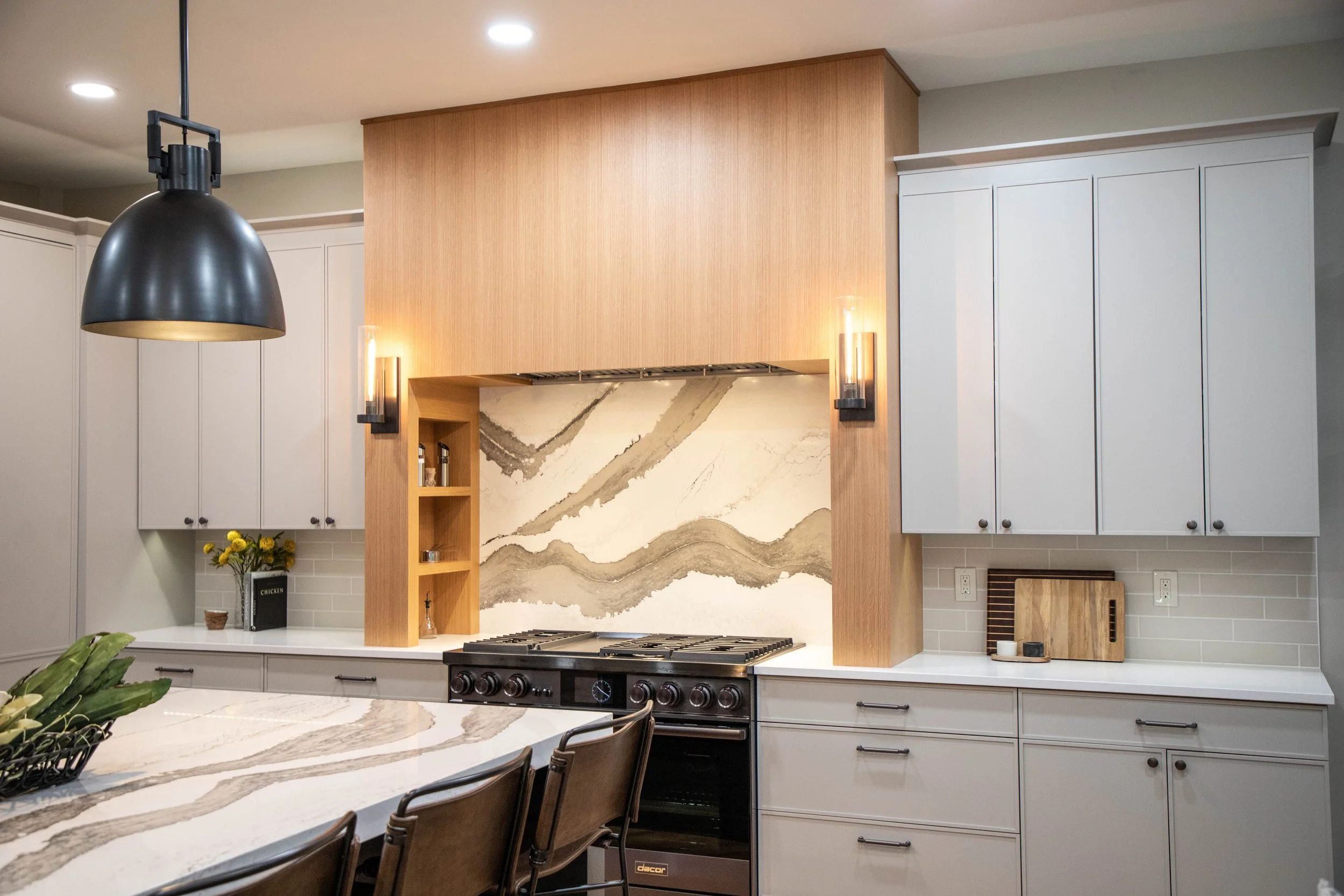 A stunning White Oak full-height range hood overlooks a chic kitchen. A Cambria quartz backsplash is the statement piece of the space.