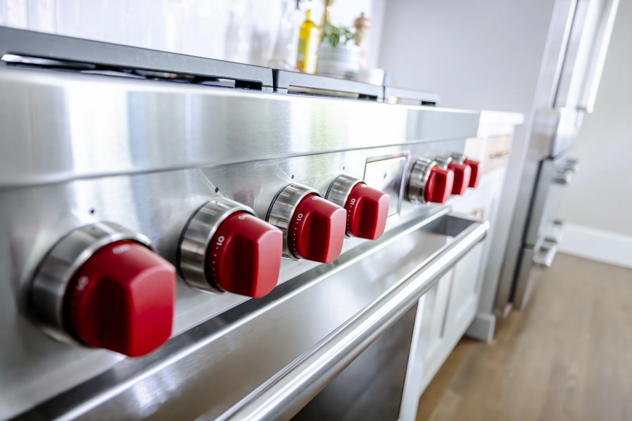 Close-up of a high-end gas range with bold red knobs, set in a modern kitchen. The sleek design and vibrant color convey a contemporary feel.