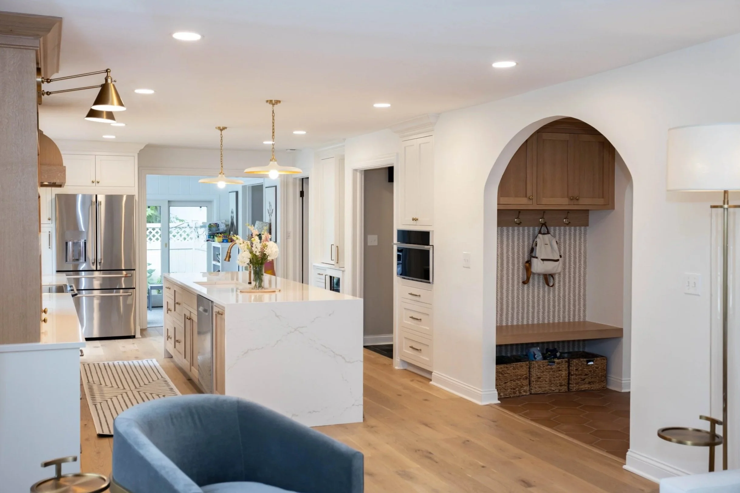A modern kitchen with a Cambria quartz waterfall island, pendant lights, and luxury appliances. Elegant seating and warm wood tones create a cozy, inviting feel.