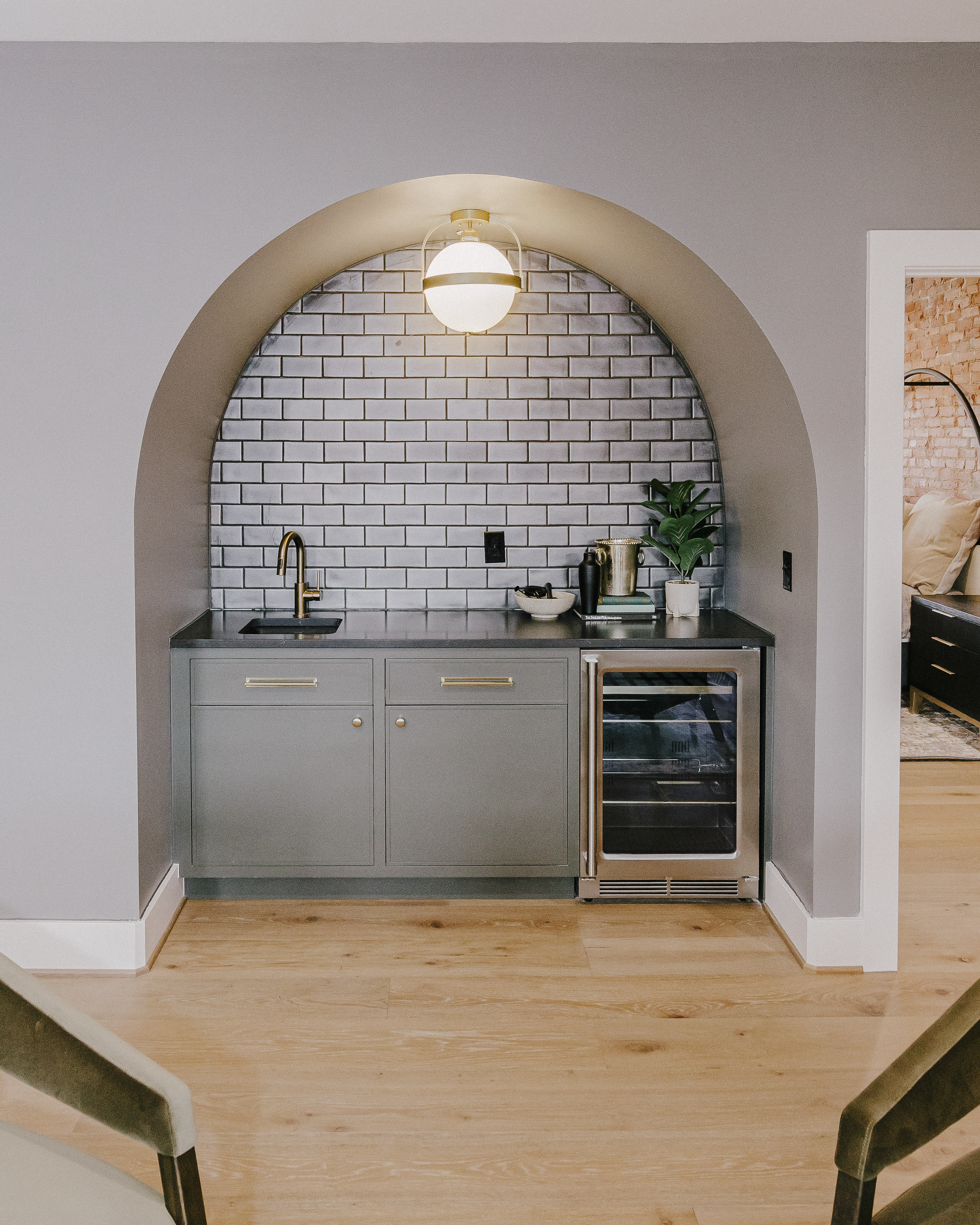 Large modern inset wet bar with slate green cabinets, black tile backsplash, globe light fixture, and beverage fridge.