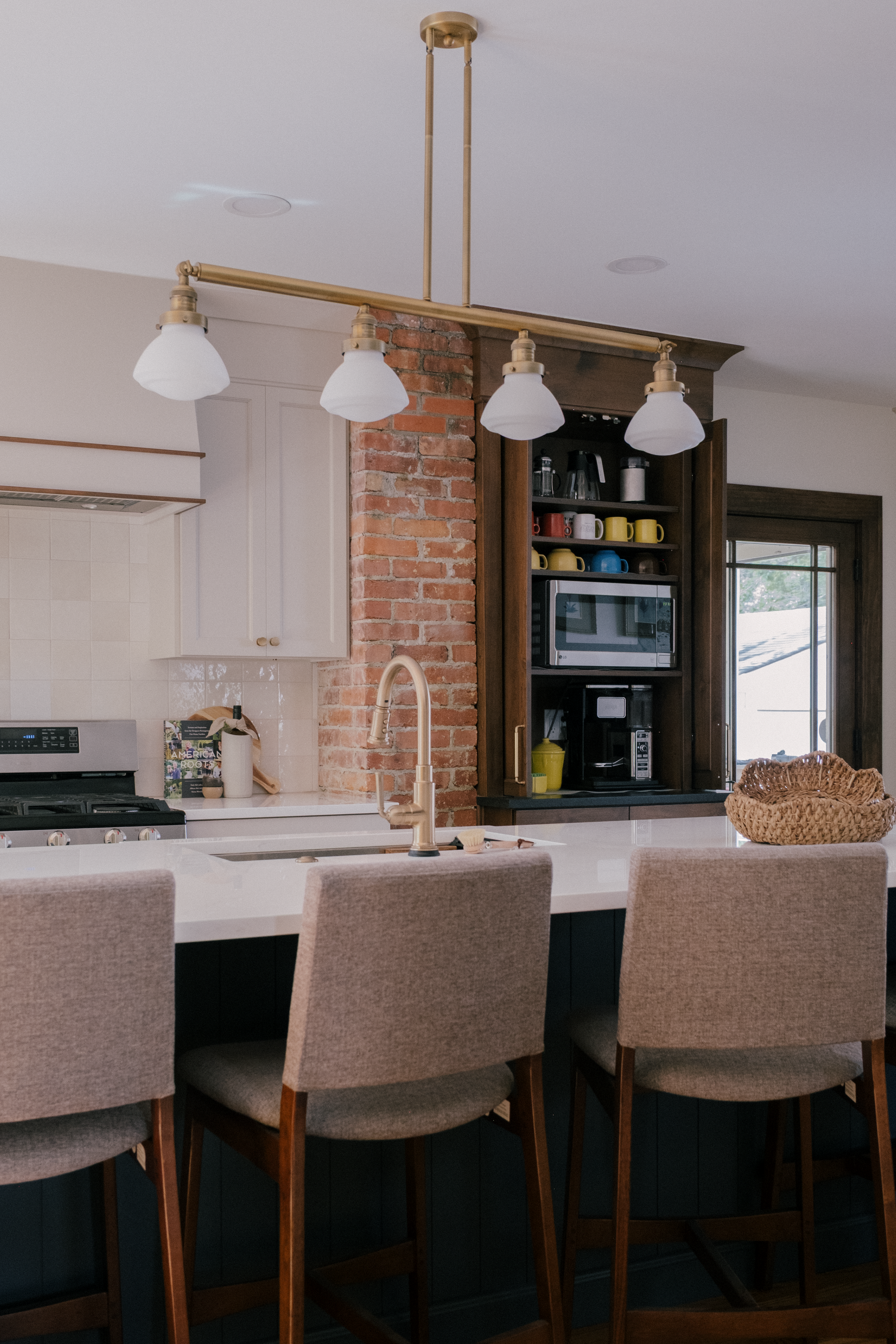 Warm historic kitchen with a Cambria quartz clad island, original brick accent wall, and coffee station hidden behind wooden pocket doors.