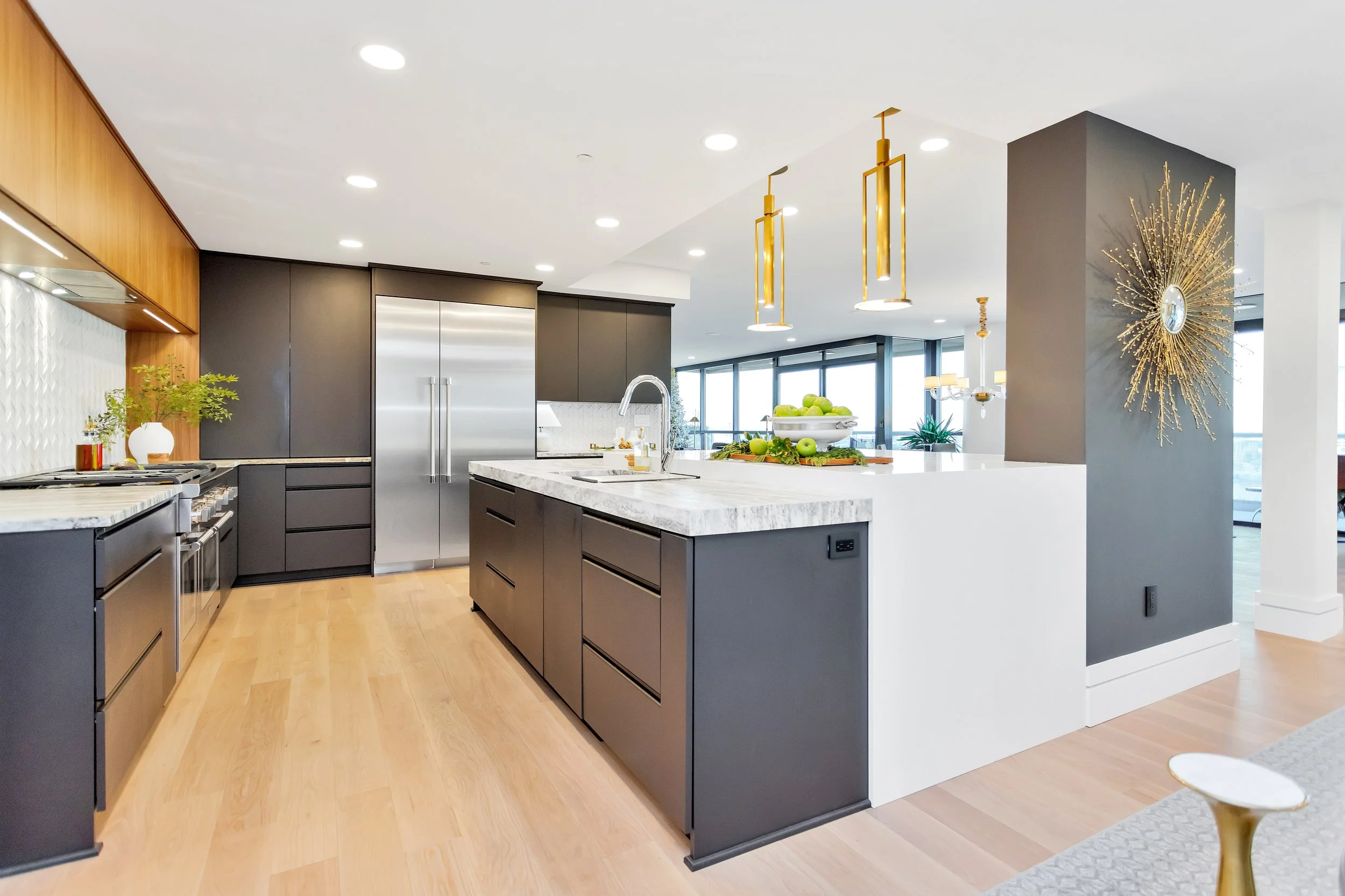 Modern kitchen with sleek dark cabinets, a quartz island, and luxury steel appliances. Bright lighting and elegant gold accents enhance the space.