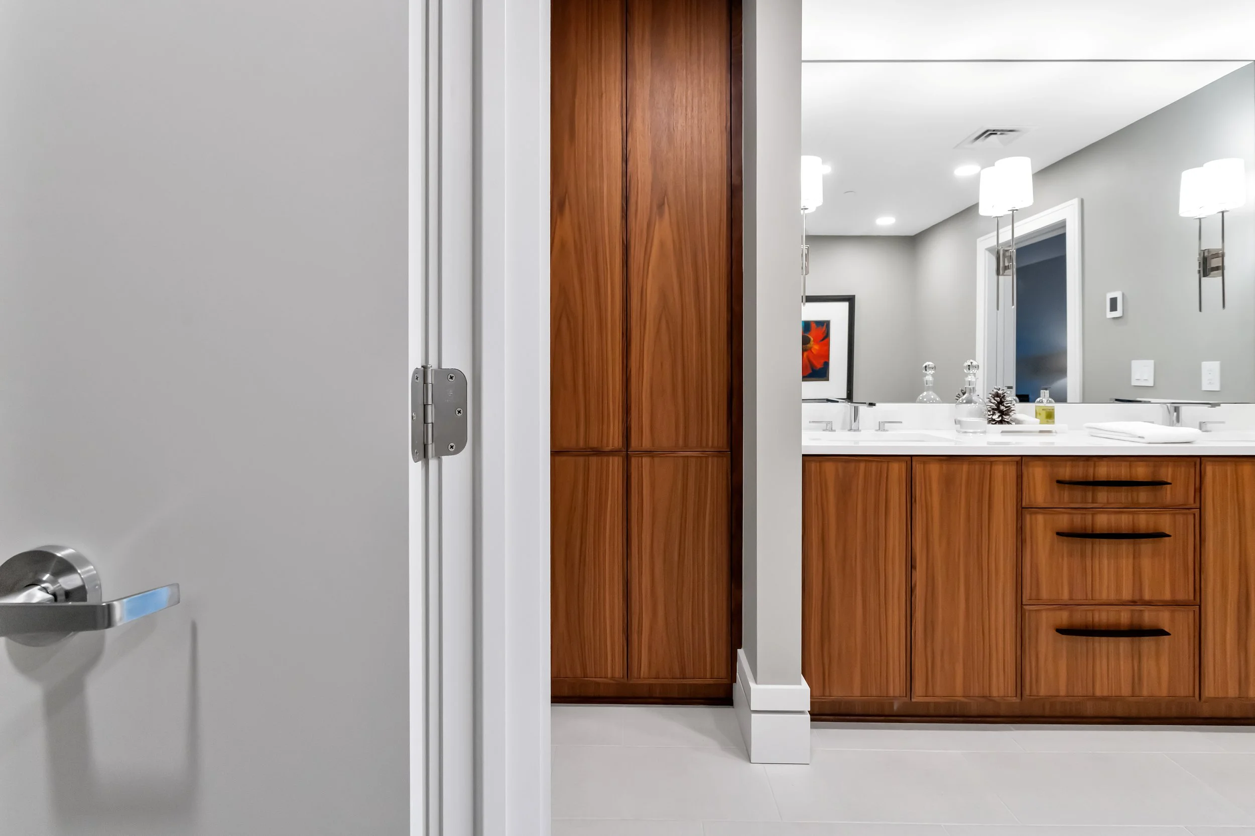 Modern bathroom with a custom wooden vanity accented with matte black handles, a large mirror, and soft lighting.