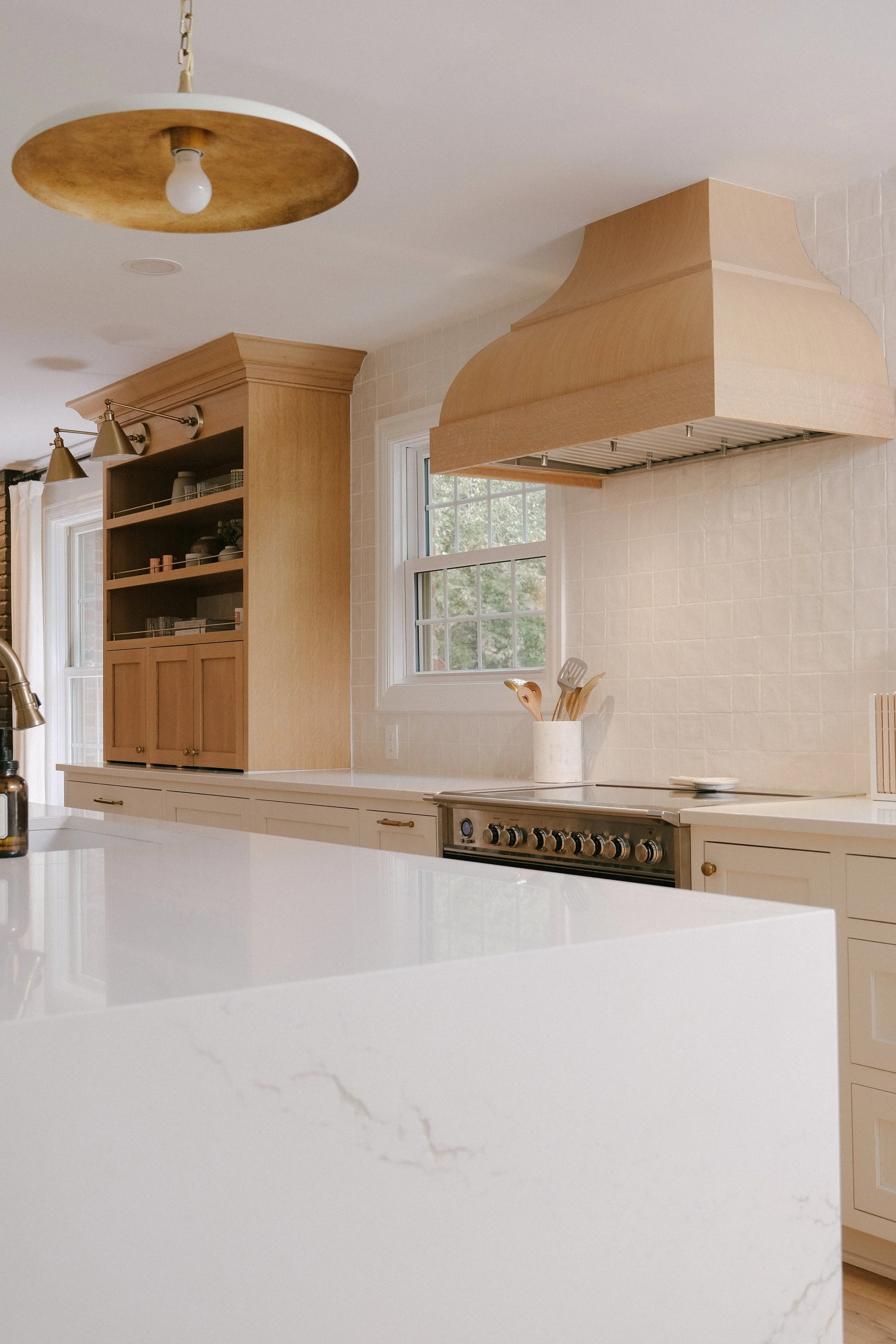 Warm, minimalist kitchen with a Cambria quartz countertop, custom stain Maple range hood and hutch, and rustic pendant lights, creating an inviting ambiance.