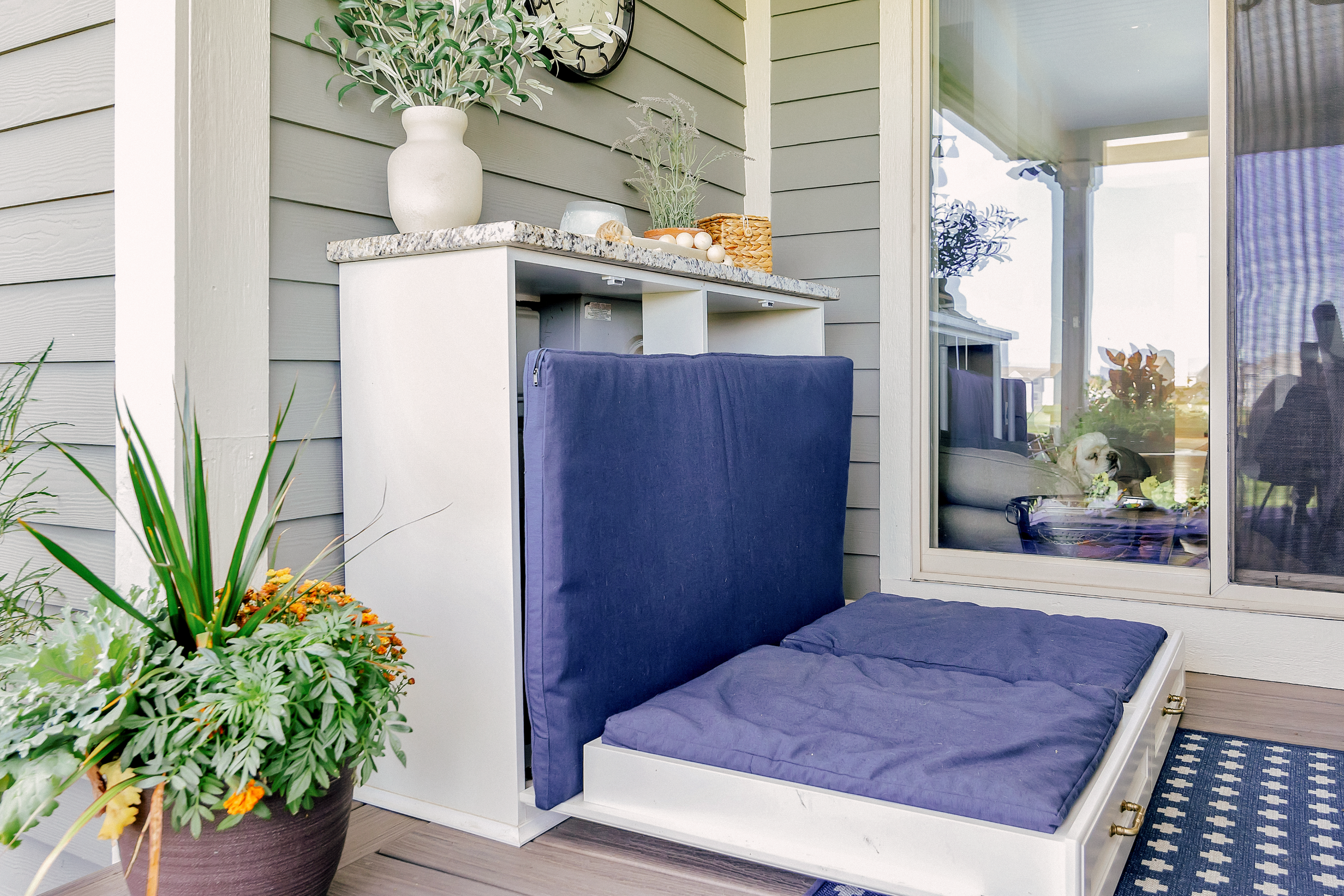 A custom outdoor cabinet with honey bronze hardware accents opens to transform into an hidden outdoor dog bed with blue cushions.