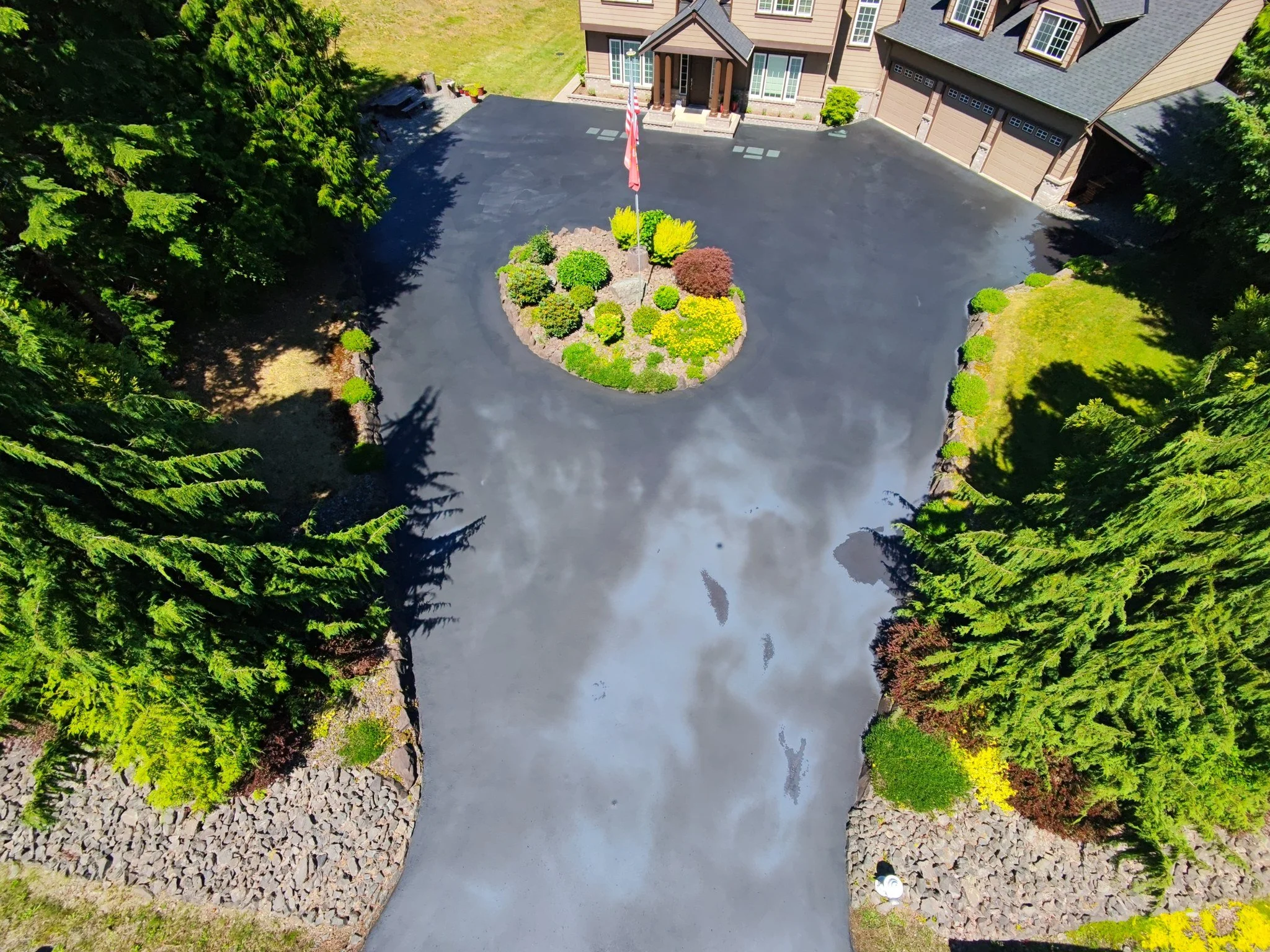 Finished driveway from above, sealed clean around the landscaped island.