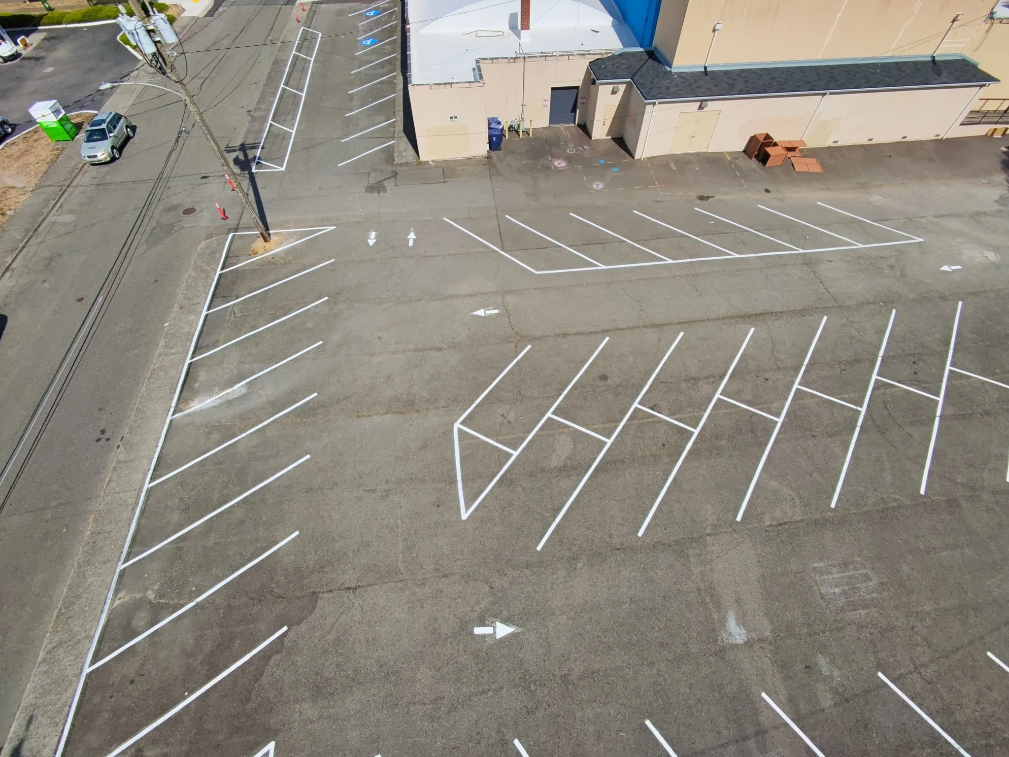 Freshly sealed parking lot from above, with new angled stall lines and painted safety hatching.