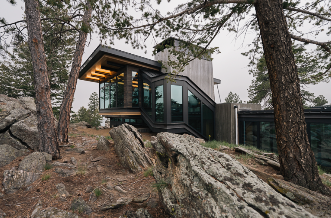 Modern house built among trees on rocky terrain with large windows and wood exterior