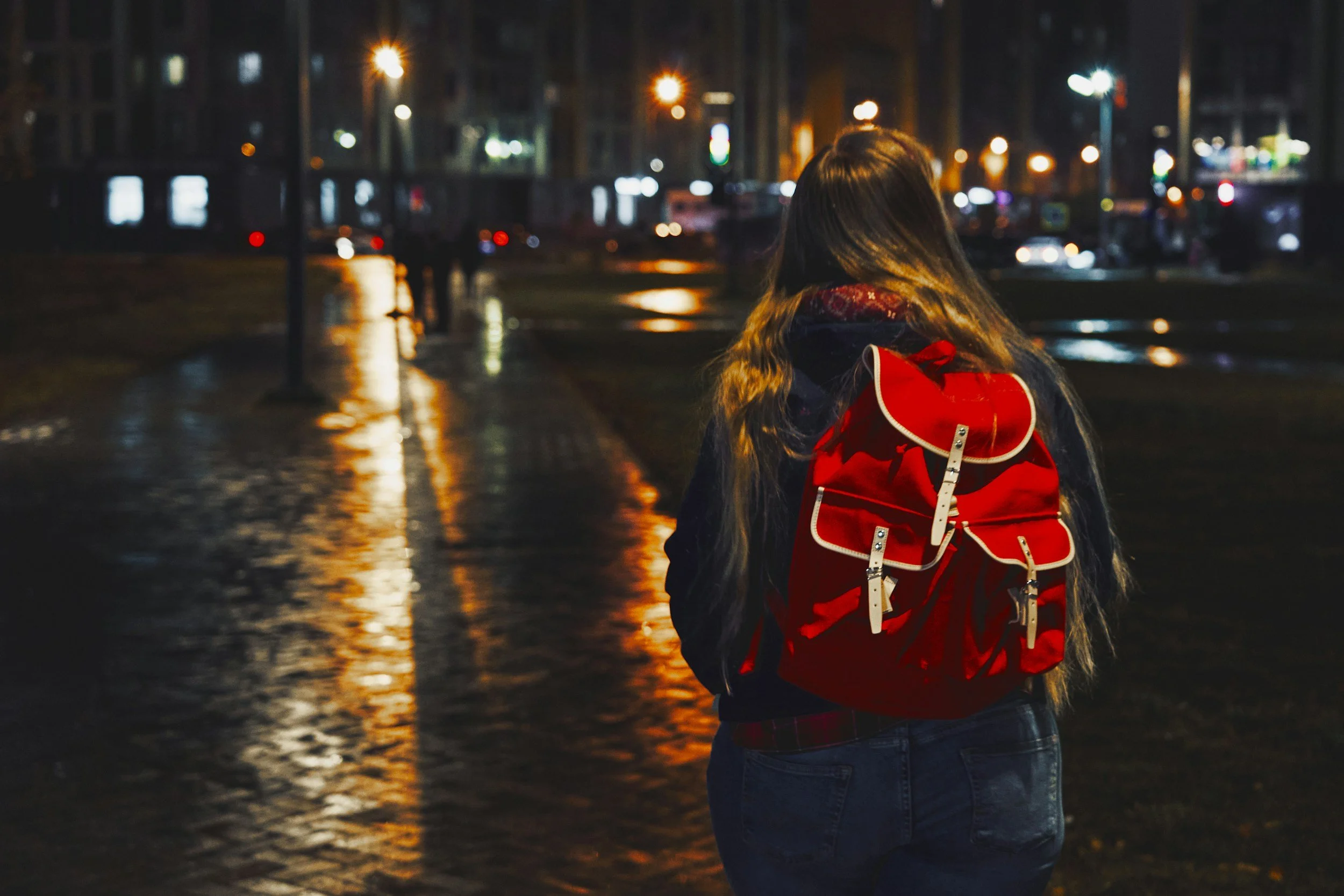 A young person looking away from the camera walking down the street with a red backpack