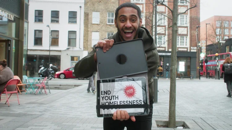 A young person holding a tablet that says ‘End Youth Homelessness - sign the petition’