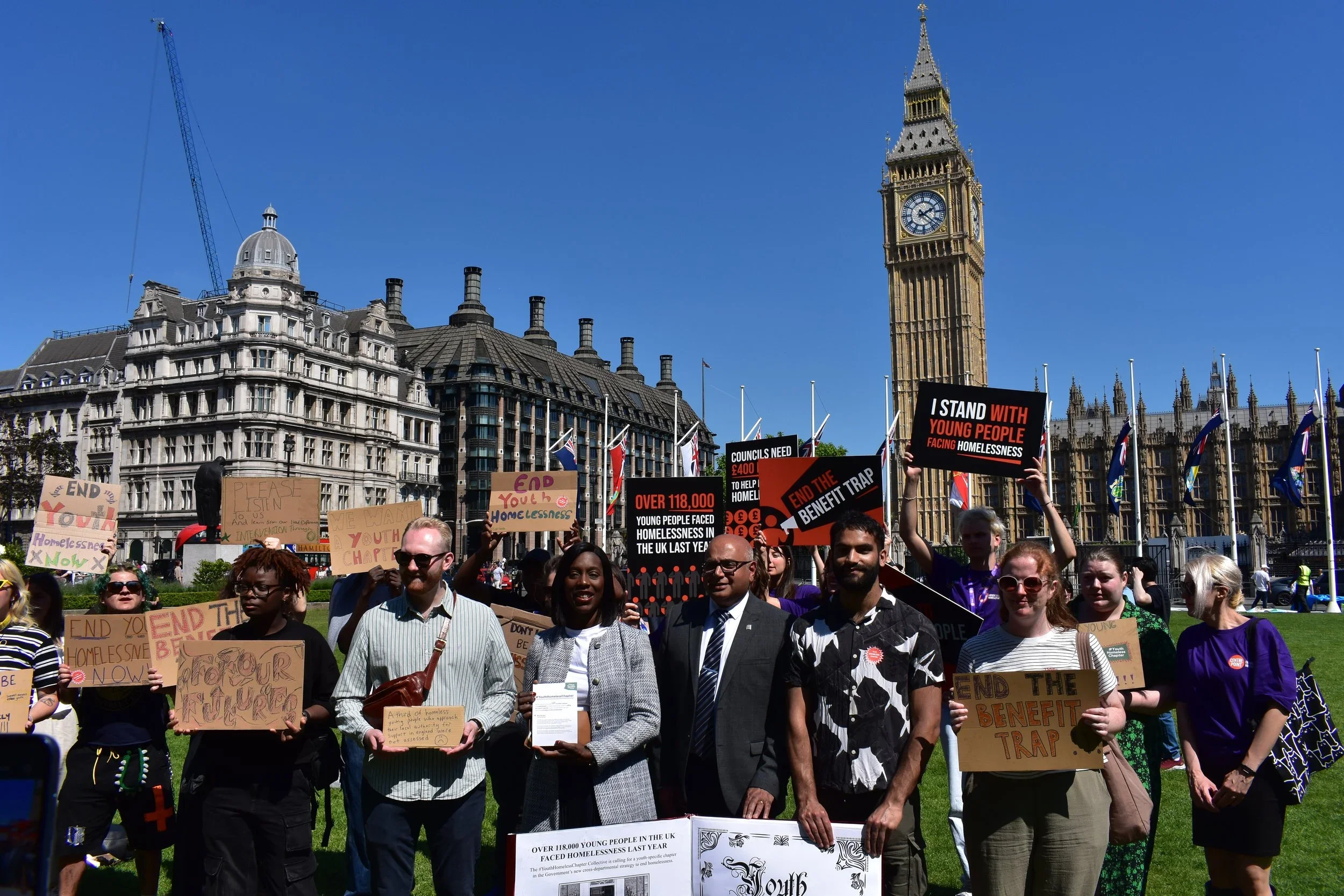  A group of young people holding signs next to MPs who are holding the Youth Chapter prop book outside Parliament 