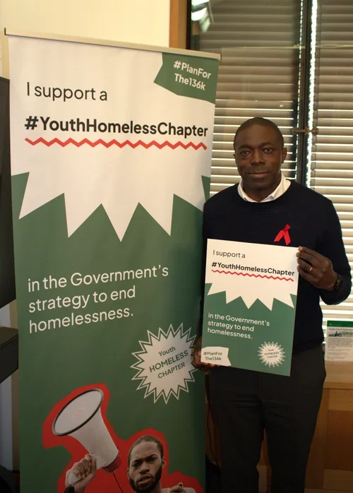Bayo Alaba MP holds a sign in support of the #Planforthe136K