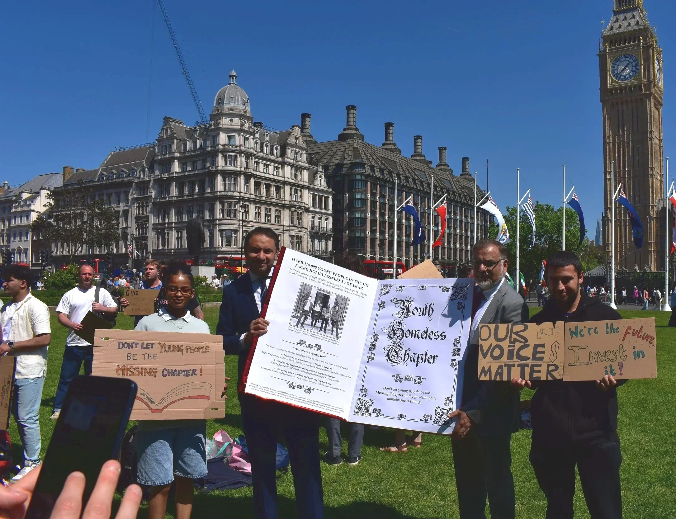 Young people and MPs holding the youth homeless chapter prop book outside parliament