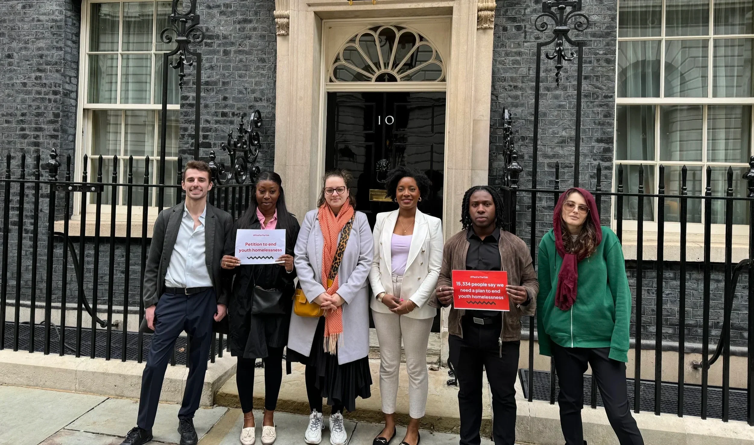Six young people and youth homeless sector members standing outside 10 downing street holding signs about their petition for a youth homelessness strategy
