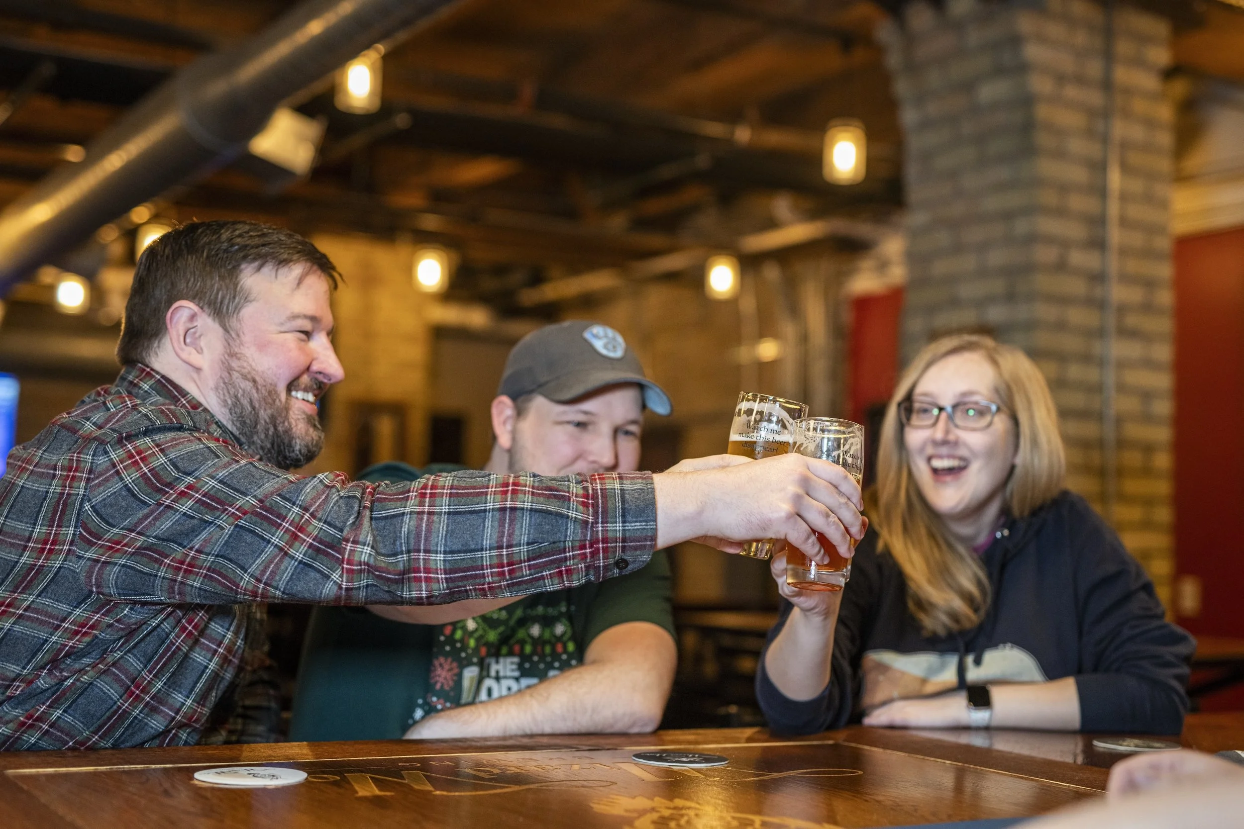 Group of friends enjoying drinks and toasting in a cozy, rustic bar with brick walls and wooden accents.