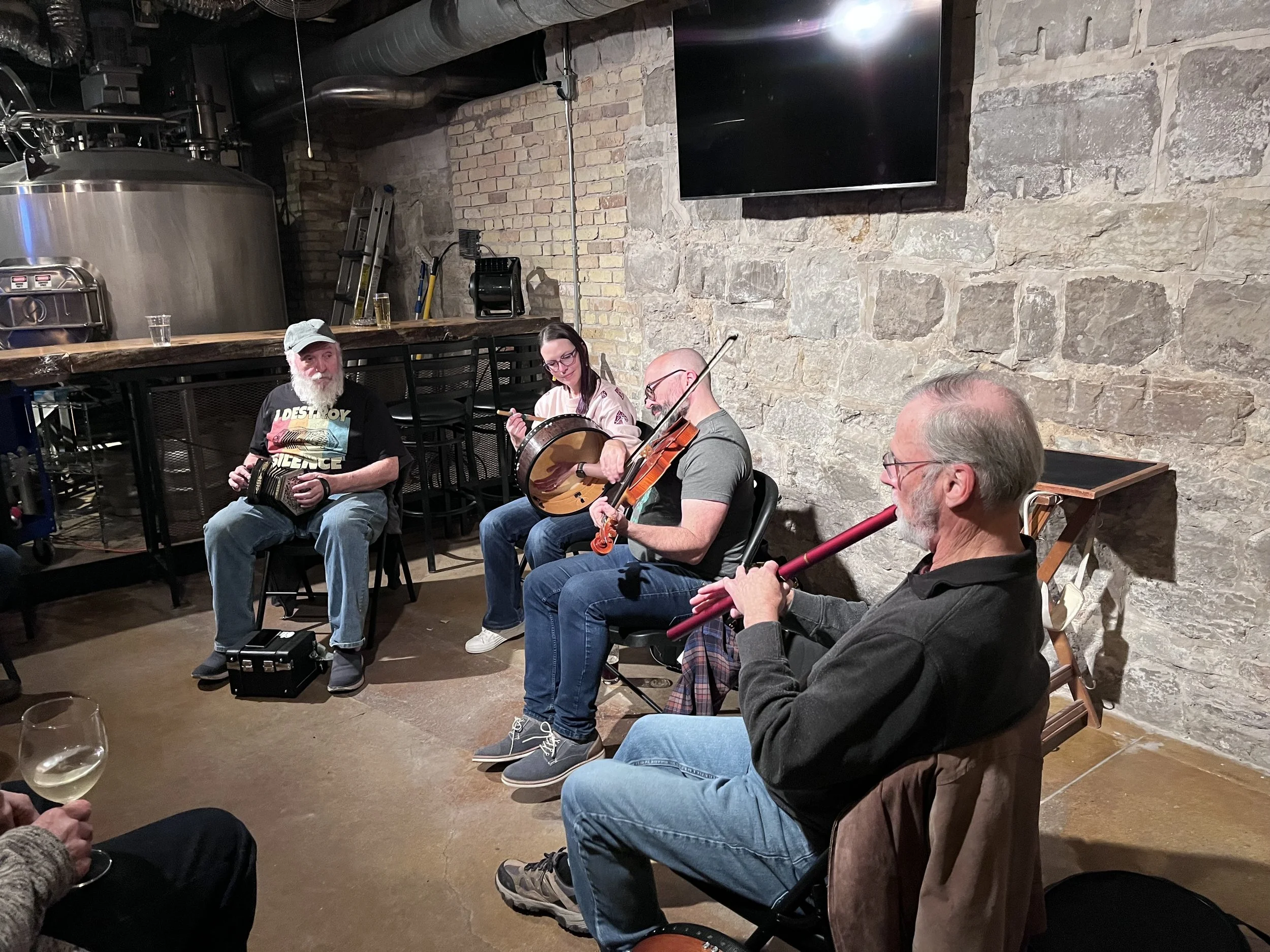A group of people sitting and playing musical instruments in a room with exposed brick and stone walls.