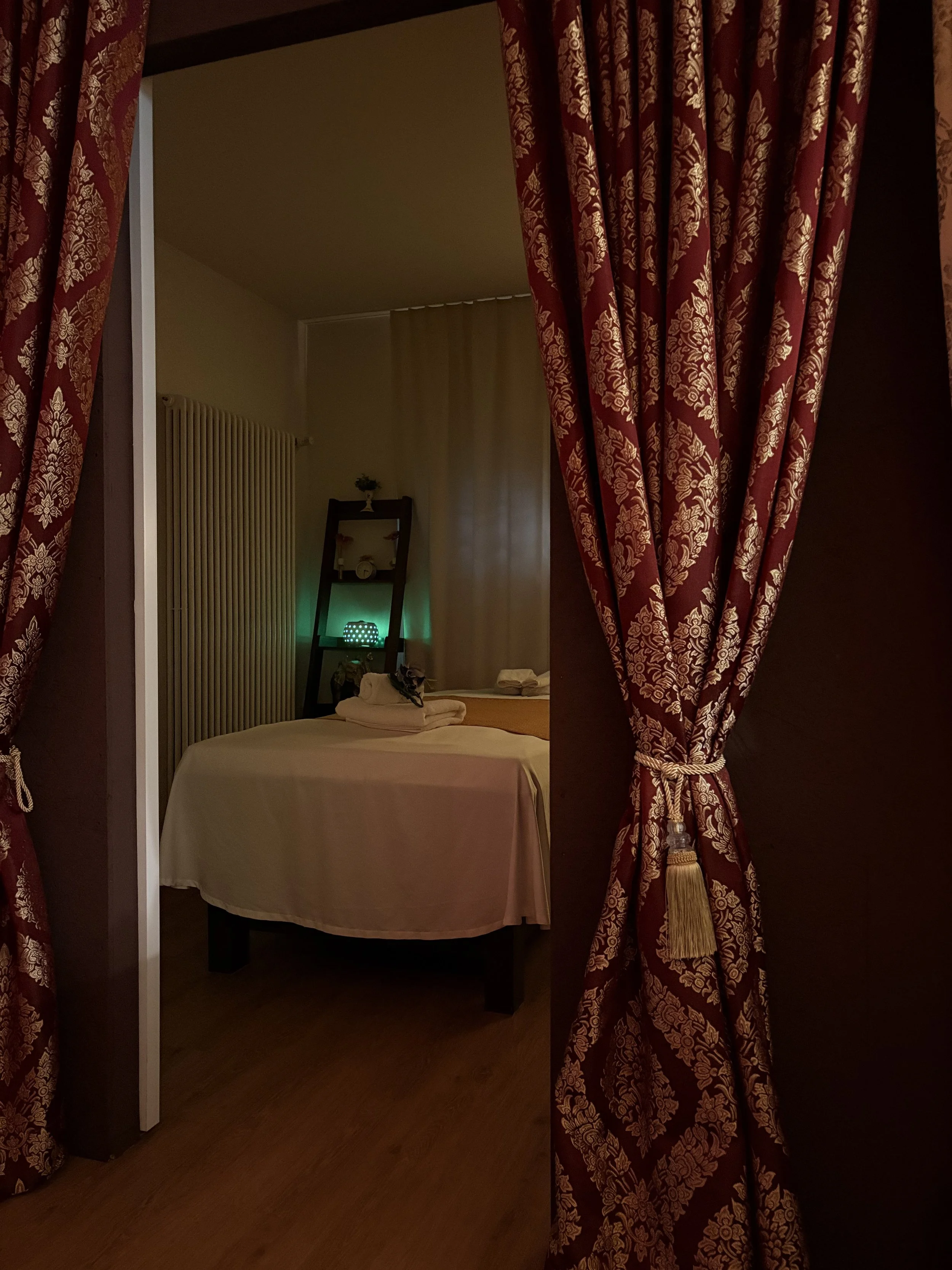 Bett in einem gemütlichen Zimmer, eingerahmt von roten, gold-ornamentierten Vorhängen.