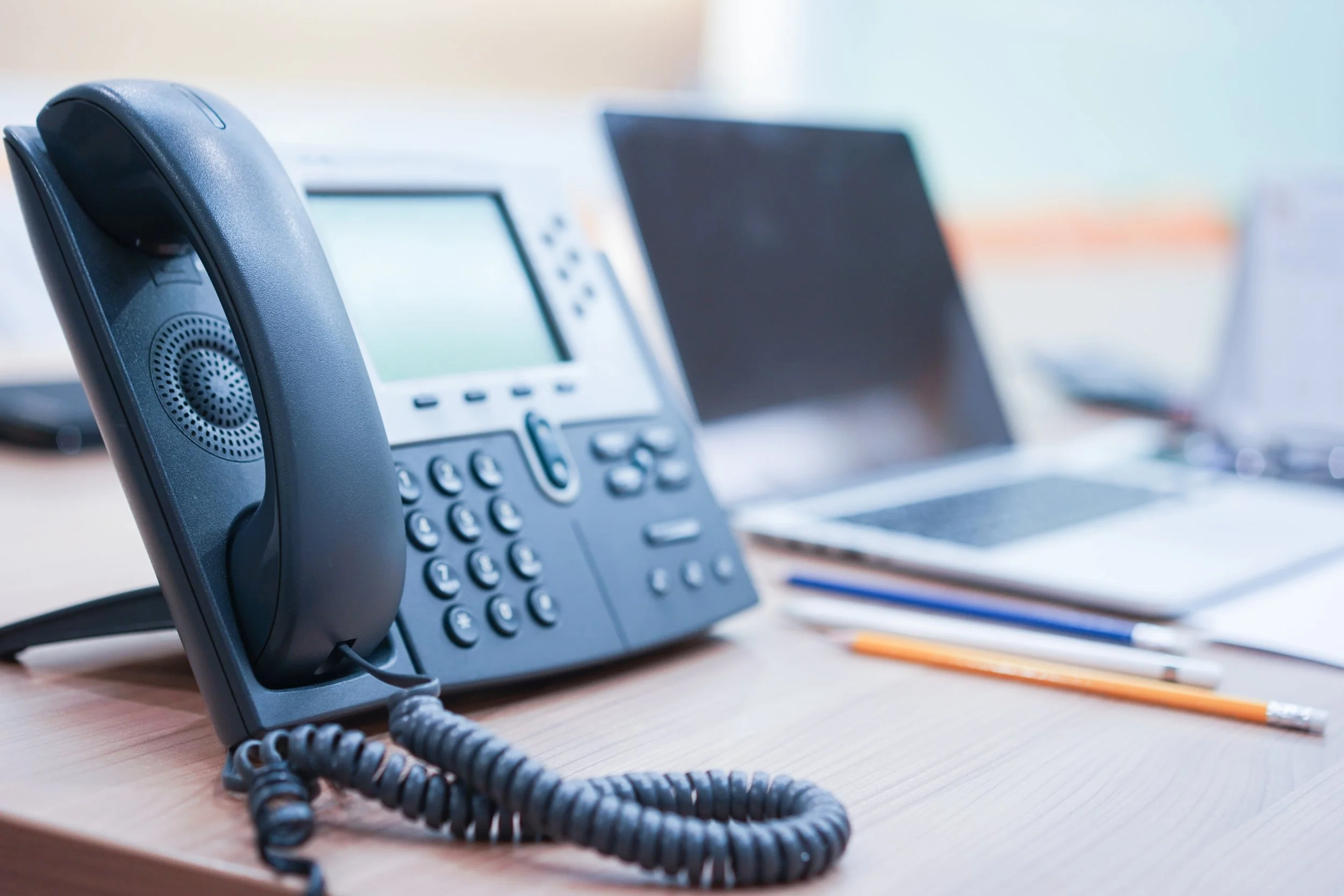 Office desk with a black landline phone, computer monitor, and open notebooks with pens.