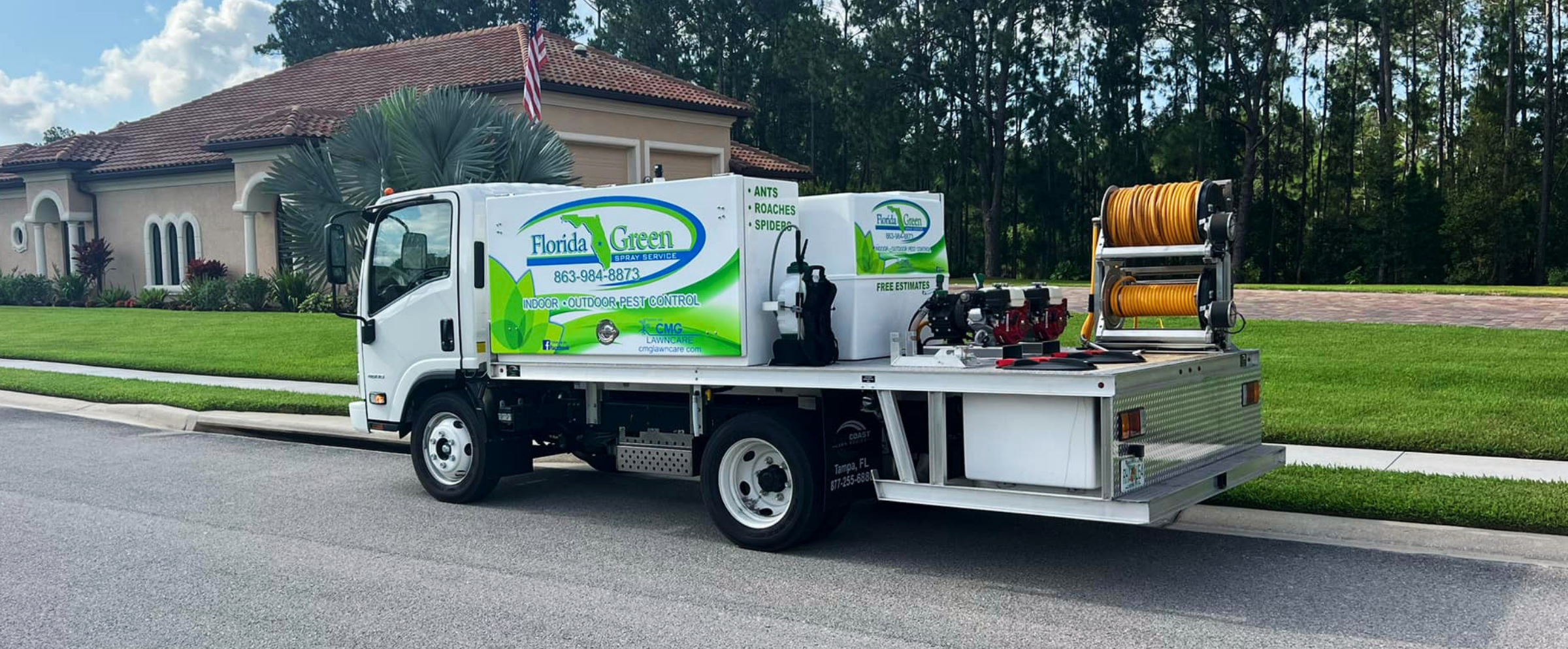 A Florida Green pest control truck parked on a suburban street in front of a house with a manicured lawn and trees. The truck has branding for indoor and outdoor pest control including ants, roaches, and spiders, with a hose reel on the back.