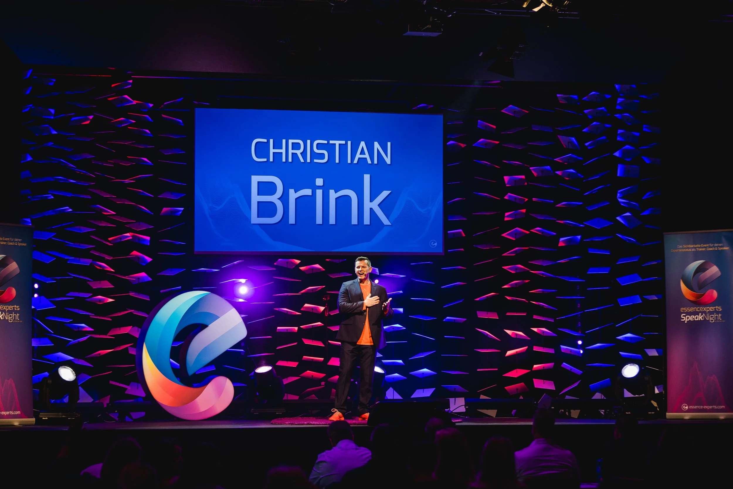 Christian Brink spricht auf einer Bühne bei der SpeakNight-Veranstaltung, im Hintergrund ein Bildschirm mit seinem Namen.