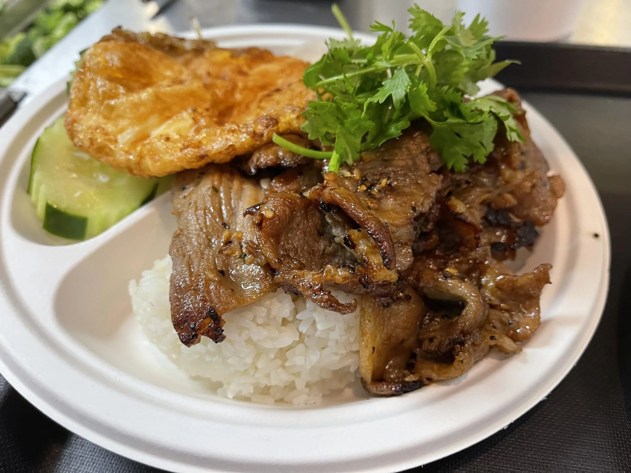 Plate of white rice topped with grilled meat, garnished with cilantro, served with cucumber slices and a fried egg.