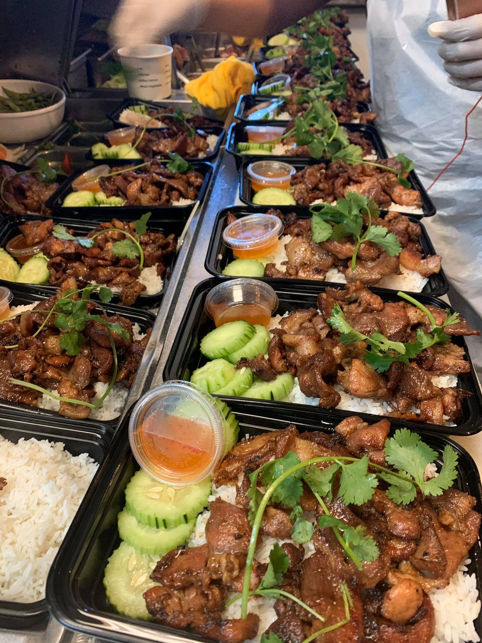 Takeout containers filled with rice, grilled meats, cucumber slices, cilantro, and small cups of sauce, ready for serving.
