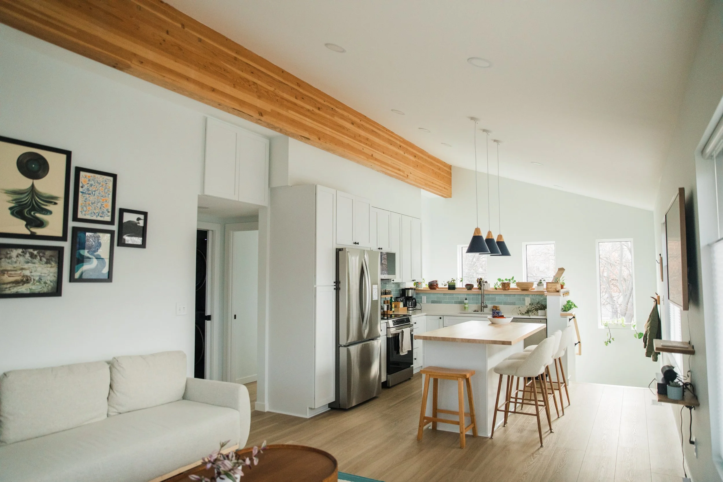 Open-concept kitchen and living room with white walls, wooden accents, and modern decor, including framed artwork on the wall and pendant lighting over the kitchen island.