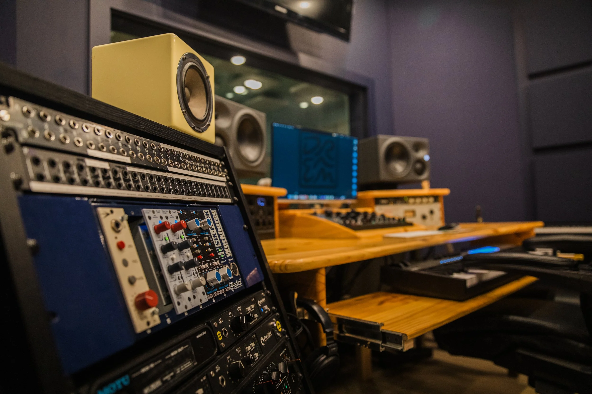 Audio production studio with speakers, audio equipment, and sound mixing console, featuring yellow, gray, and wooden elements.