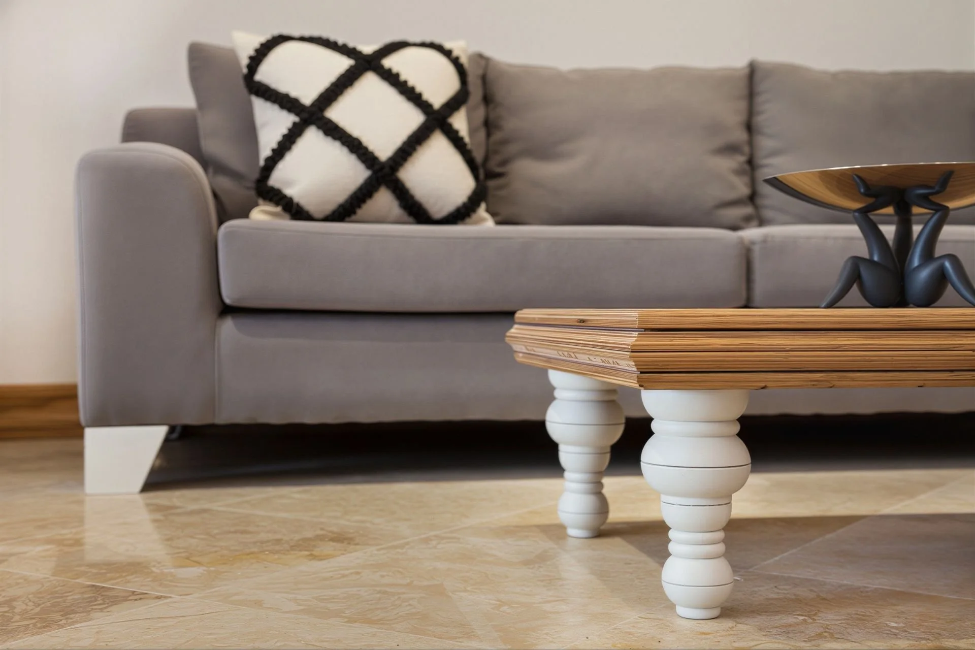 Living room with gray sofa, black and white patterned pillow, wooden coffee table with white legs, and a decorative black figurine sculpture. Light-colored tiled floor.