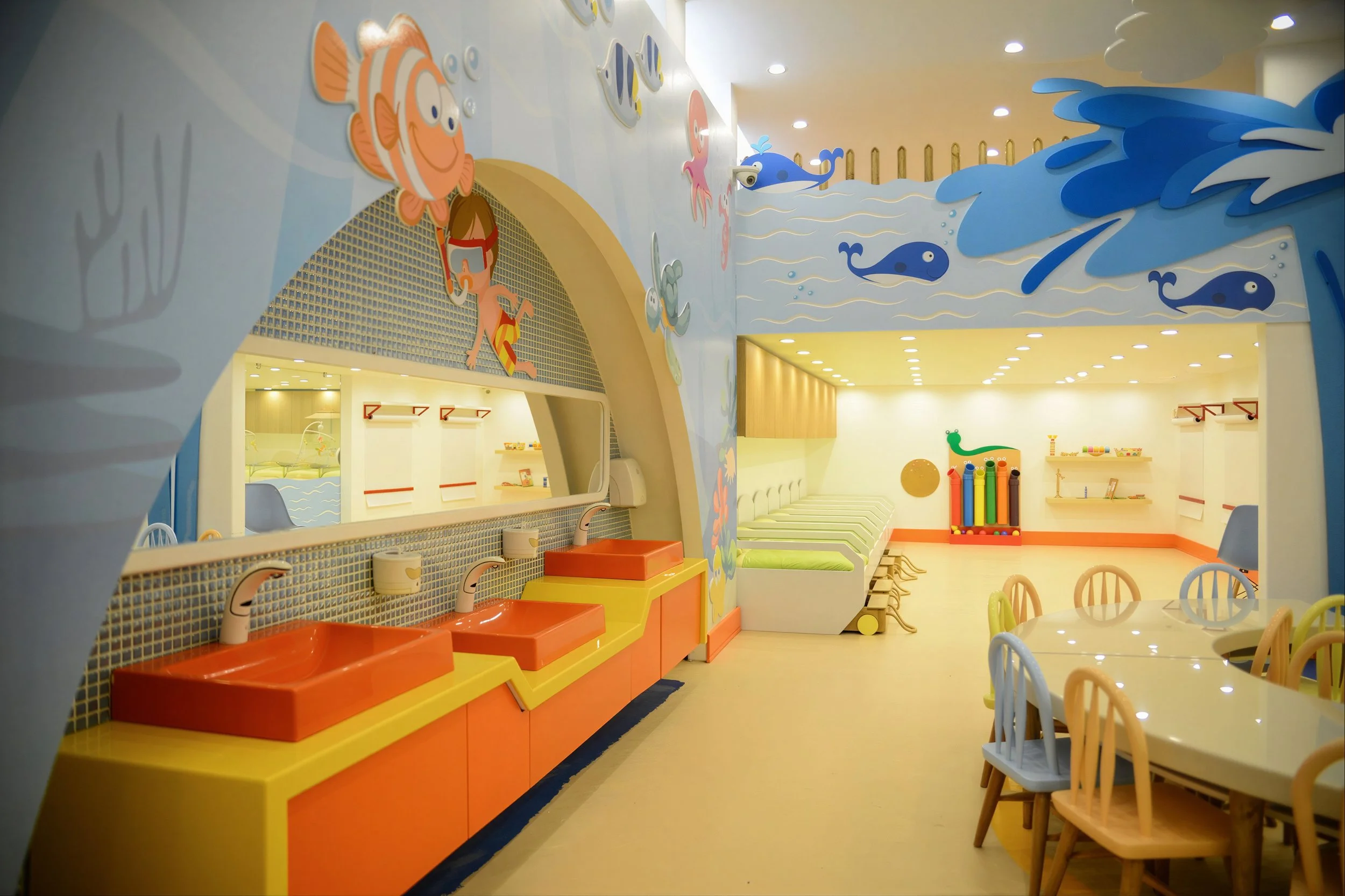 Colorful children's playroom with whale and fish decorations, play sinks, tables, and chairs.