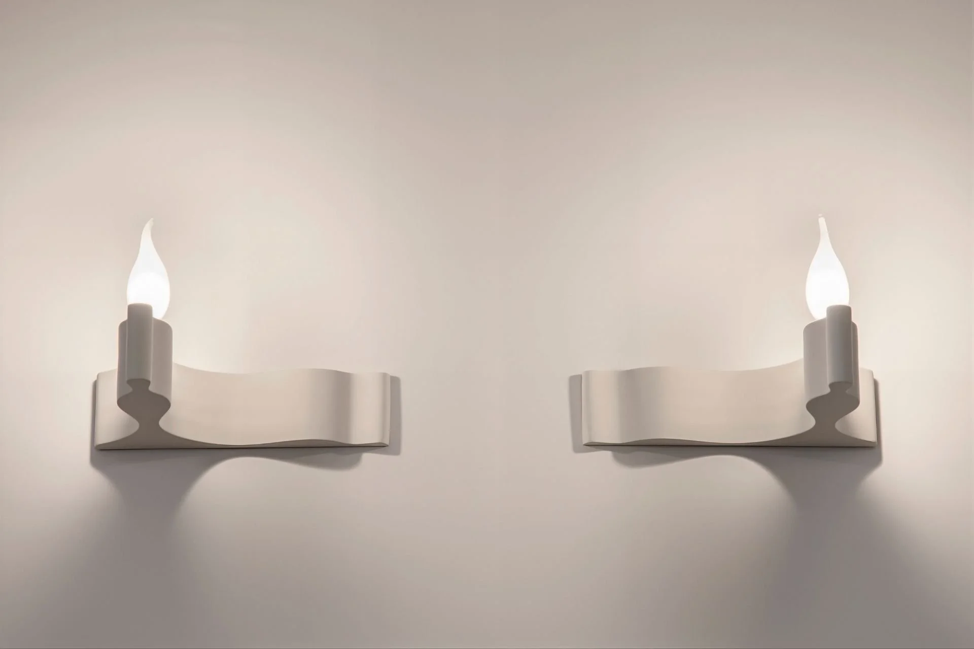 Wall-mounted modern white sconces with a curvy design, each holding a small flame-shaped light bulb