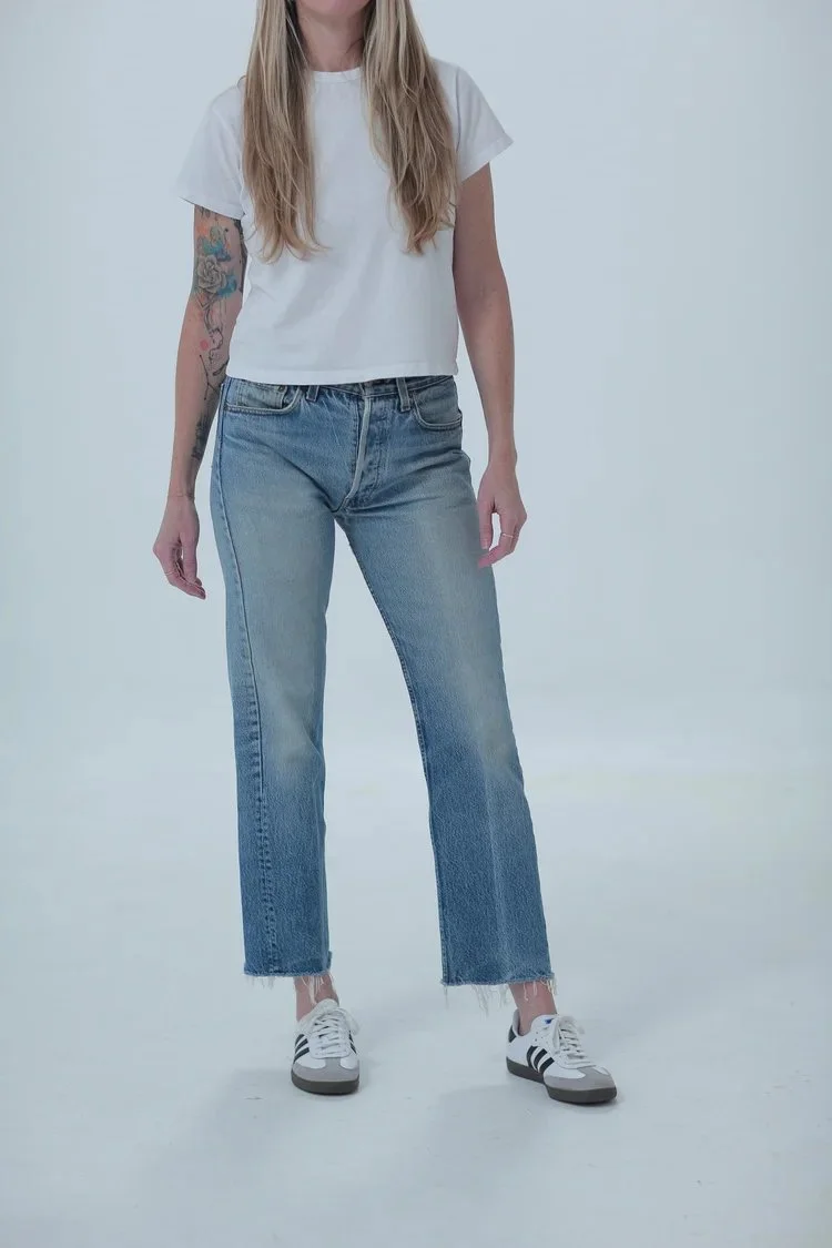 Levi's 501 classic medium wash, fitted with cropped raw hem, front view with hip leaning
