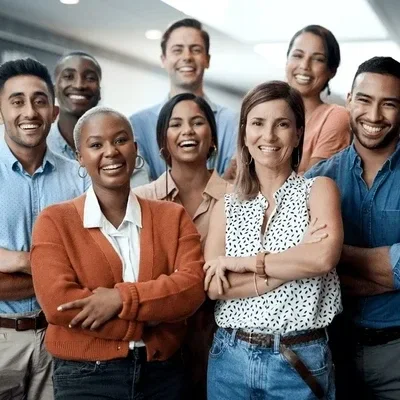 Group of eight diverse happy people standing closely together in an office, smiling at the camera.