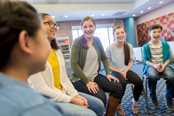 A group of five teenagers sitting in a circle and chatting in a brightly lit room.