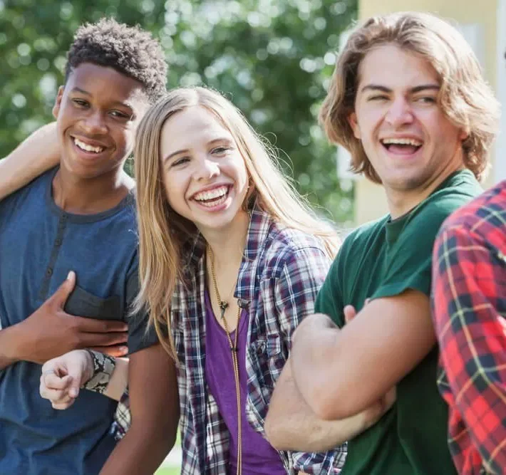 Four young friends laughing and smiling outdoors on a sunny day.