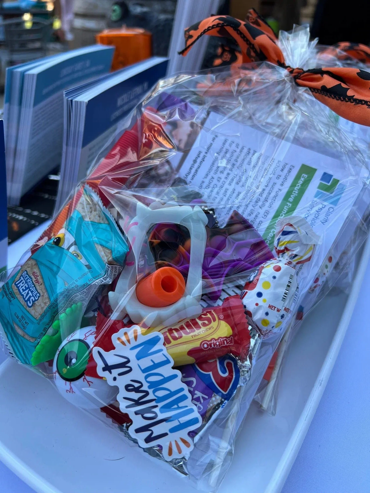 A clear plastic bag filled with various pieces of candy, including a pack of Rice Krispies Treats, a Gummy Worms package, and other assorted candies, resting inside a white container.