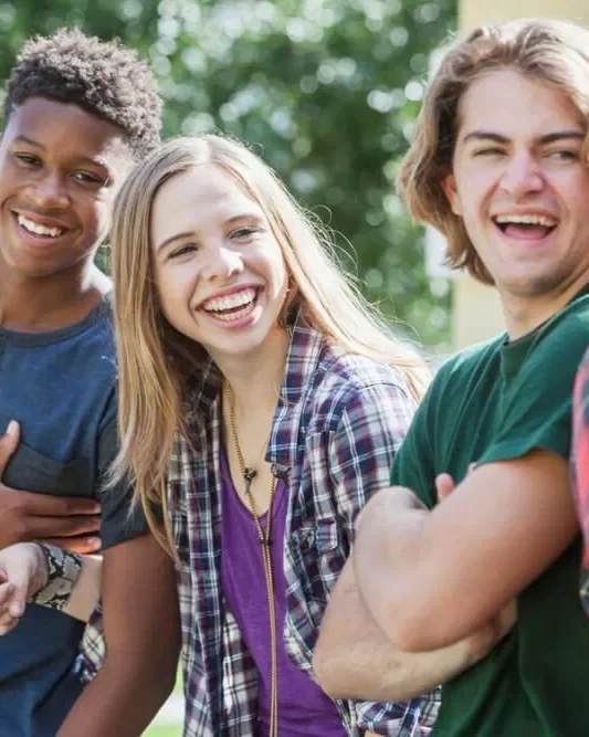 Three young friends smiling outdoors with a green, blurred background.